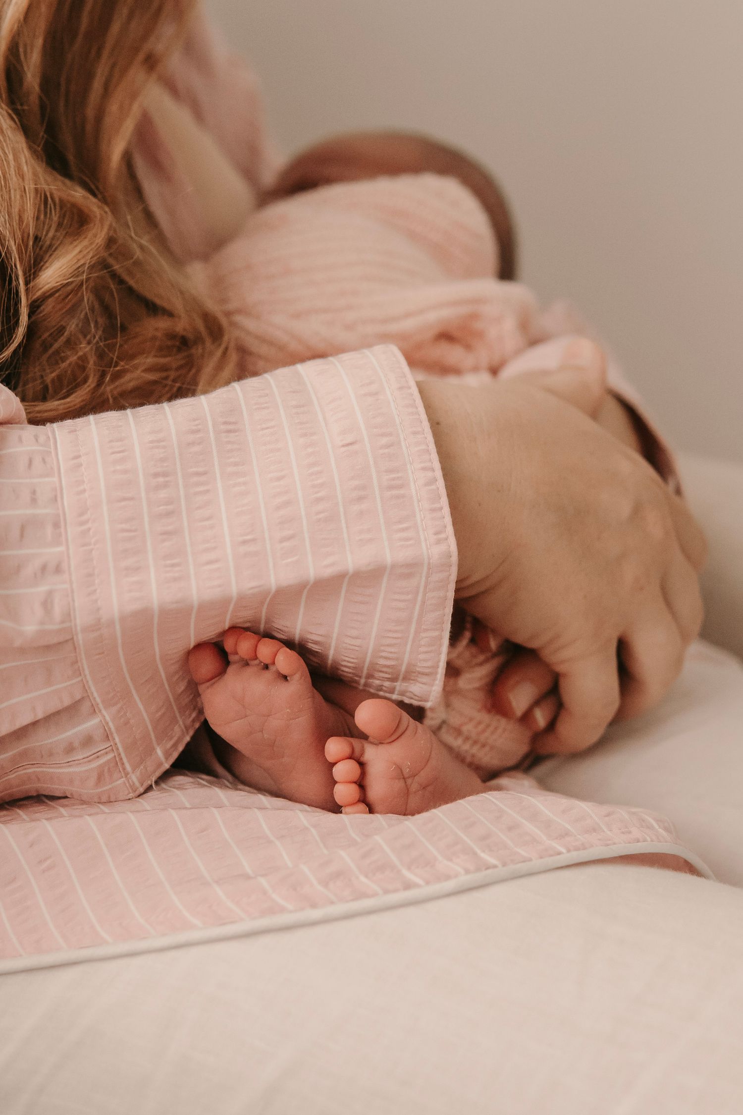 Close up of tiny newborn baby feet peeking out from soft pink blanket.