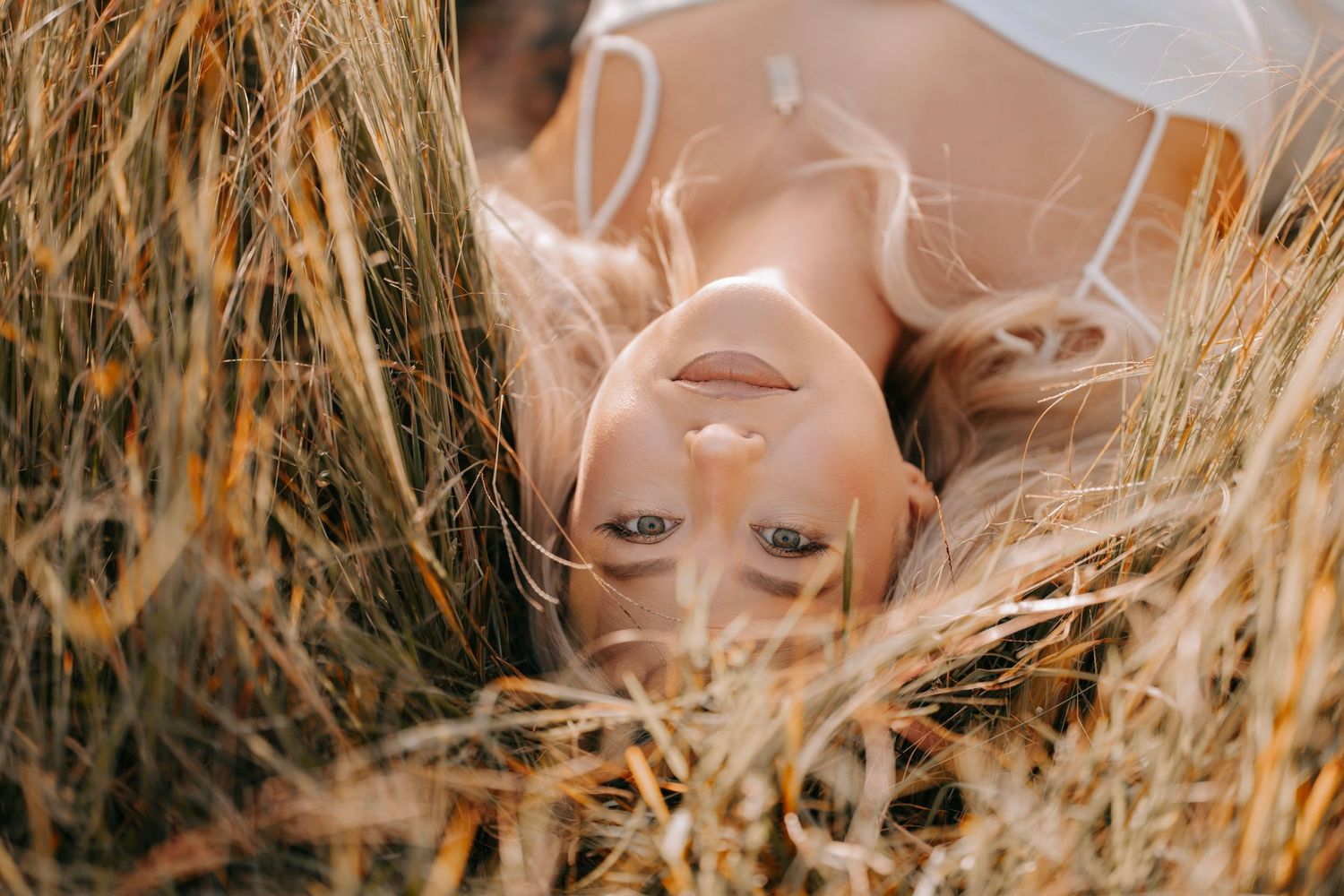 Blonde woman lying upside down in golden wheat field with eyes closed peacefully.