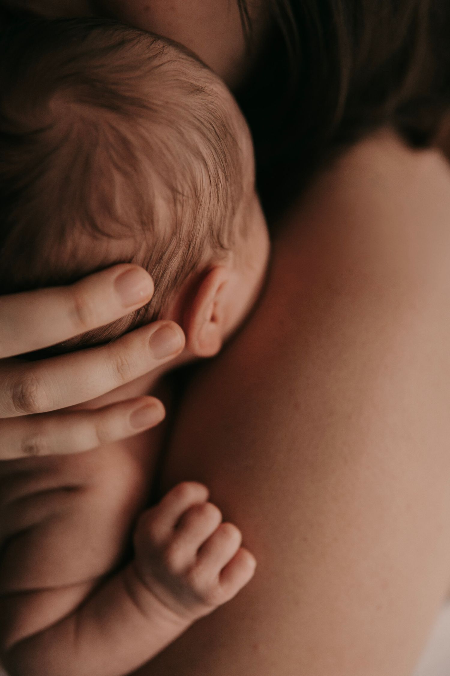 A newborn baby cradled gently in a parent's arms, showing tiny fingers and delicate features up close.