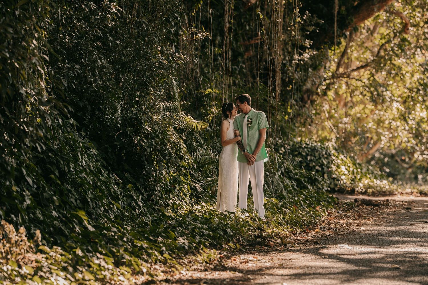 Romantic couple sharing a tender moment on a shaded path surrounded by lush green foliage.