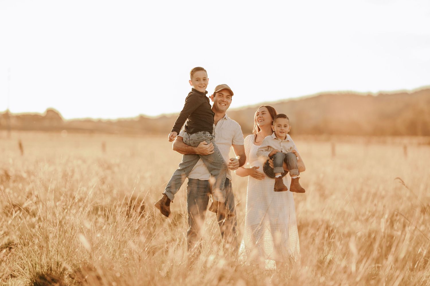 Happy family of four standing in golden wheat field during sunset.
