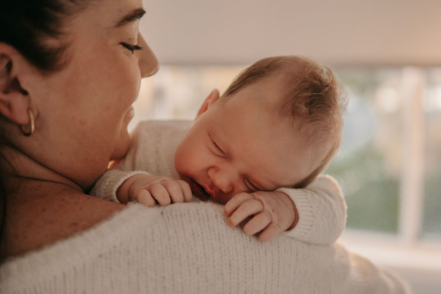Mother gazing lovingly at sleeping newborn baby resting peacefully on her shoulder.