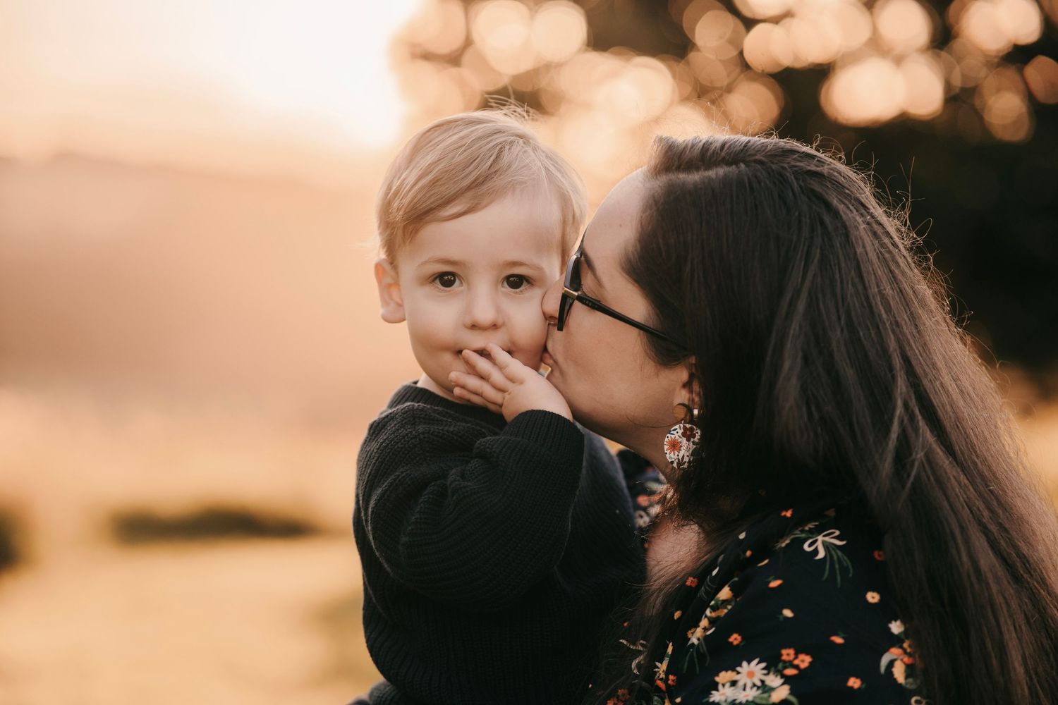 A mother kisses her toddler son on the cheek during a golden hour outdoor photo session.