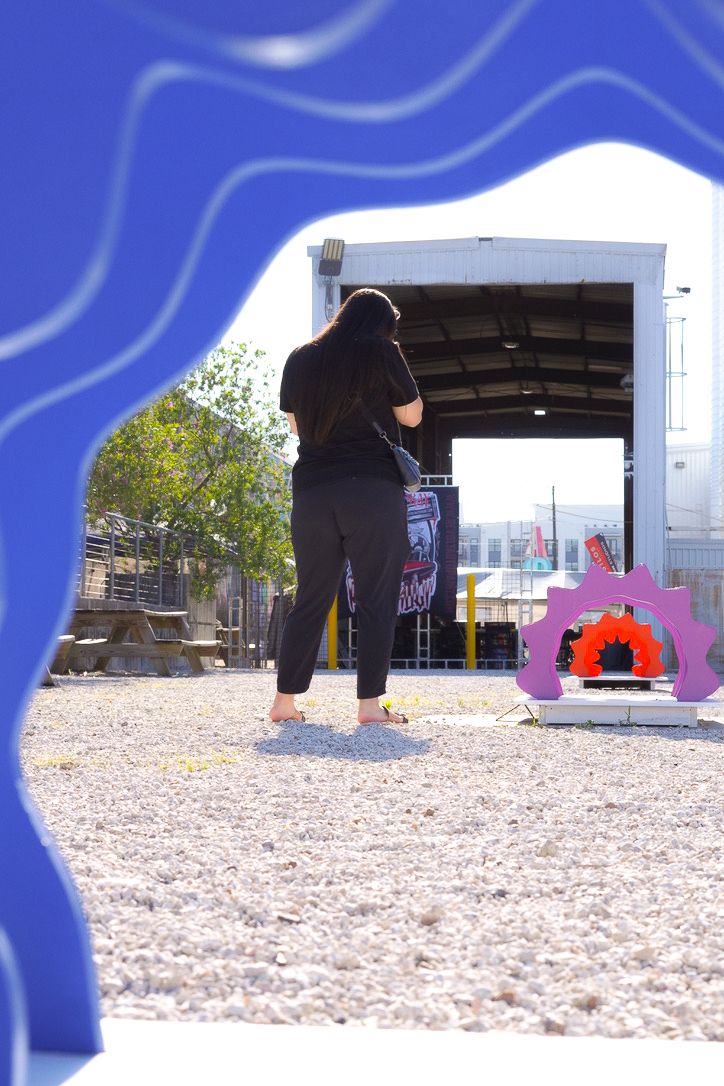 Person standing near an arched art instillation  and event trailer in a sunny outdoor space