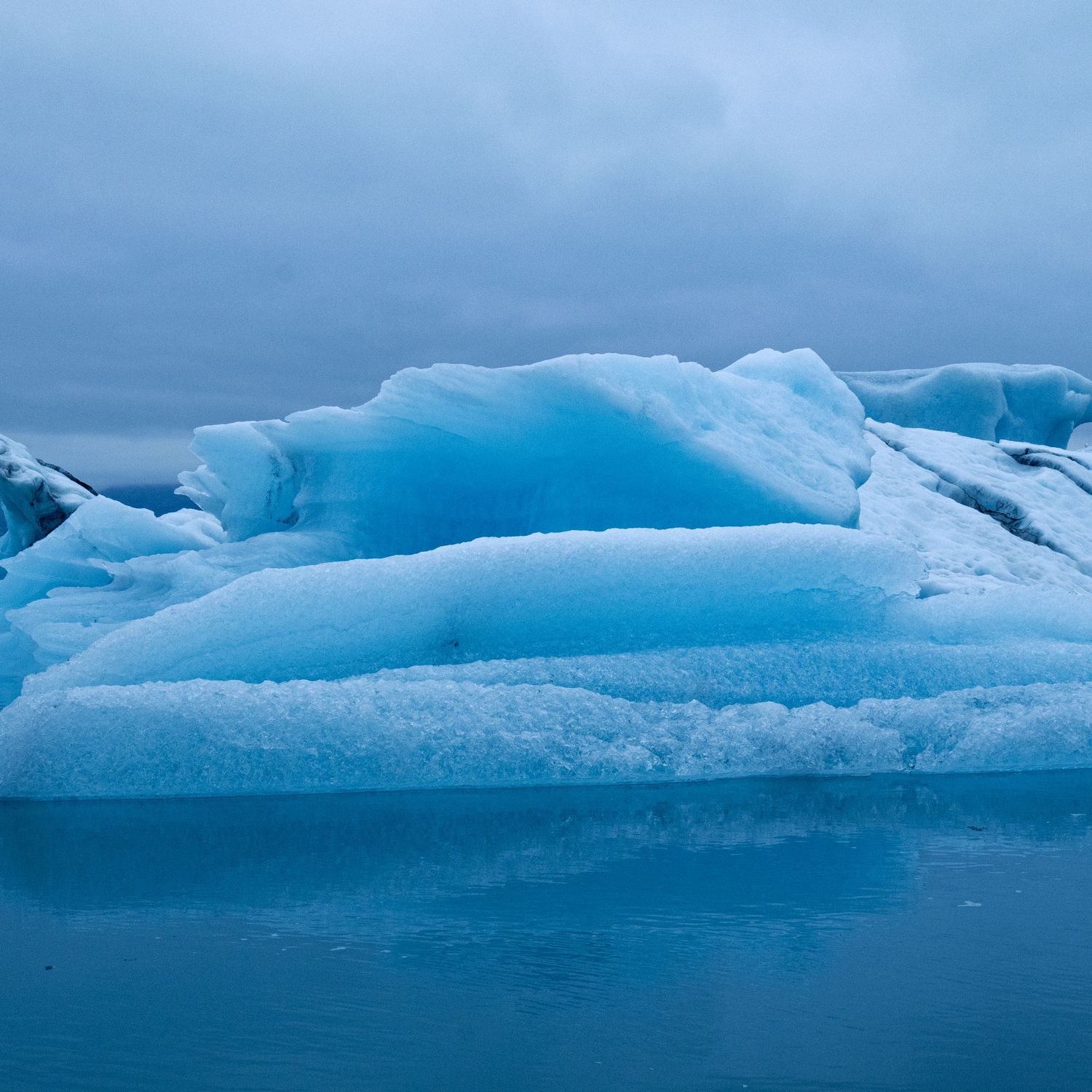 Blue icebergs floating in still water beneath a cloudy, moody sky