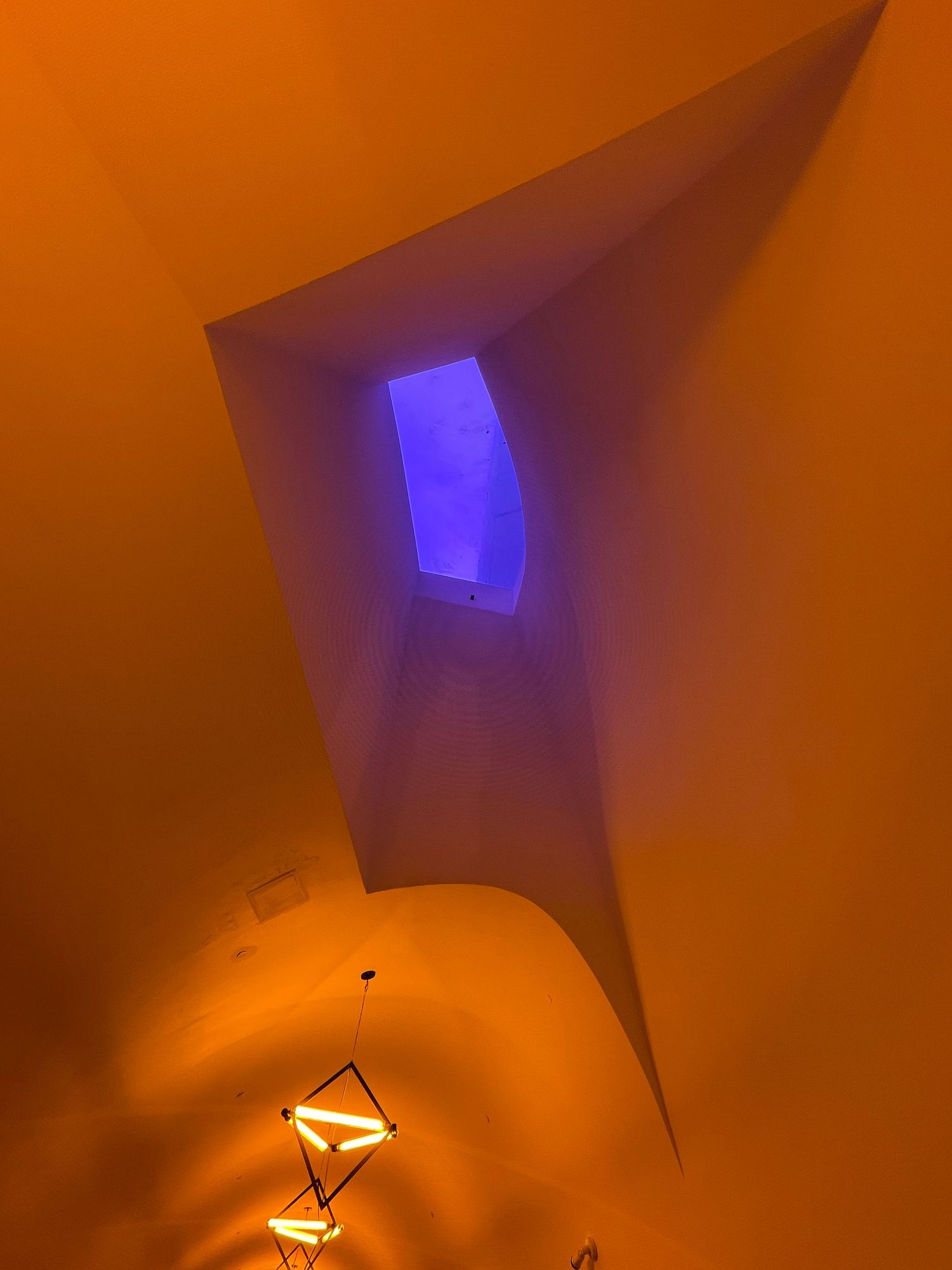 Dramatic orange ceiling with angular lines, glowing blue accent light, and chandelier