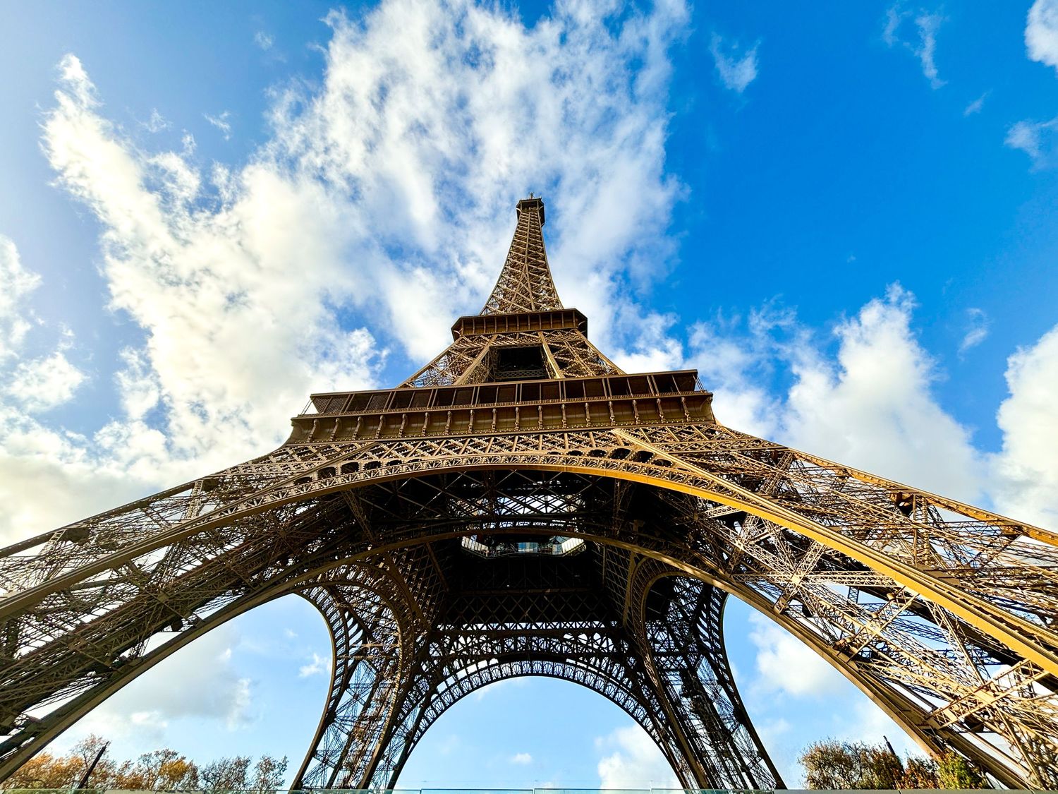 Upward view of the Eiffel Tower framed by bright blue sky and scattered clouds