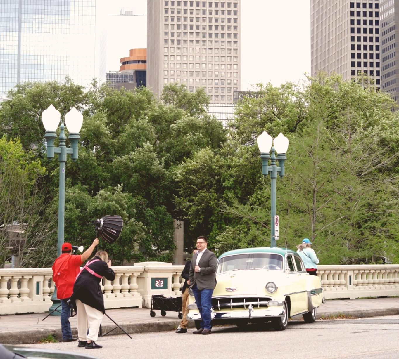 Vintage car photoshoot on city bridge with people posing and Houston skyline in background
