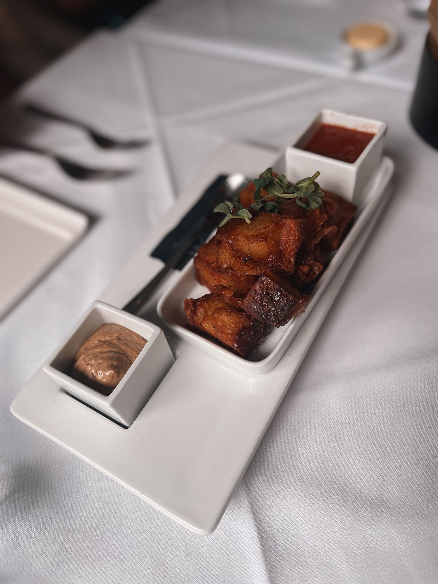 Appetizer trio with dipping sauces in a sleek white tray on fine dining table