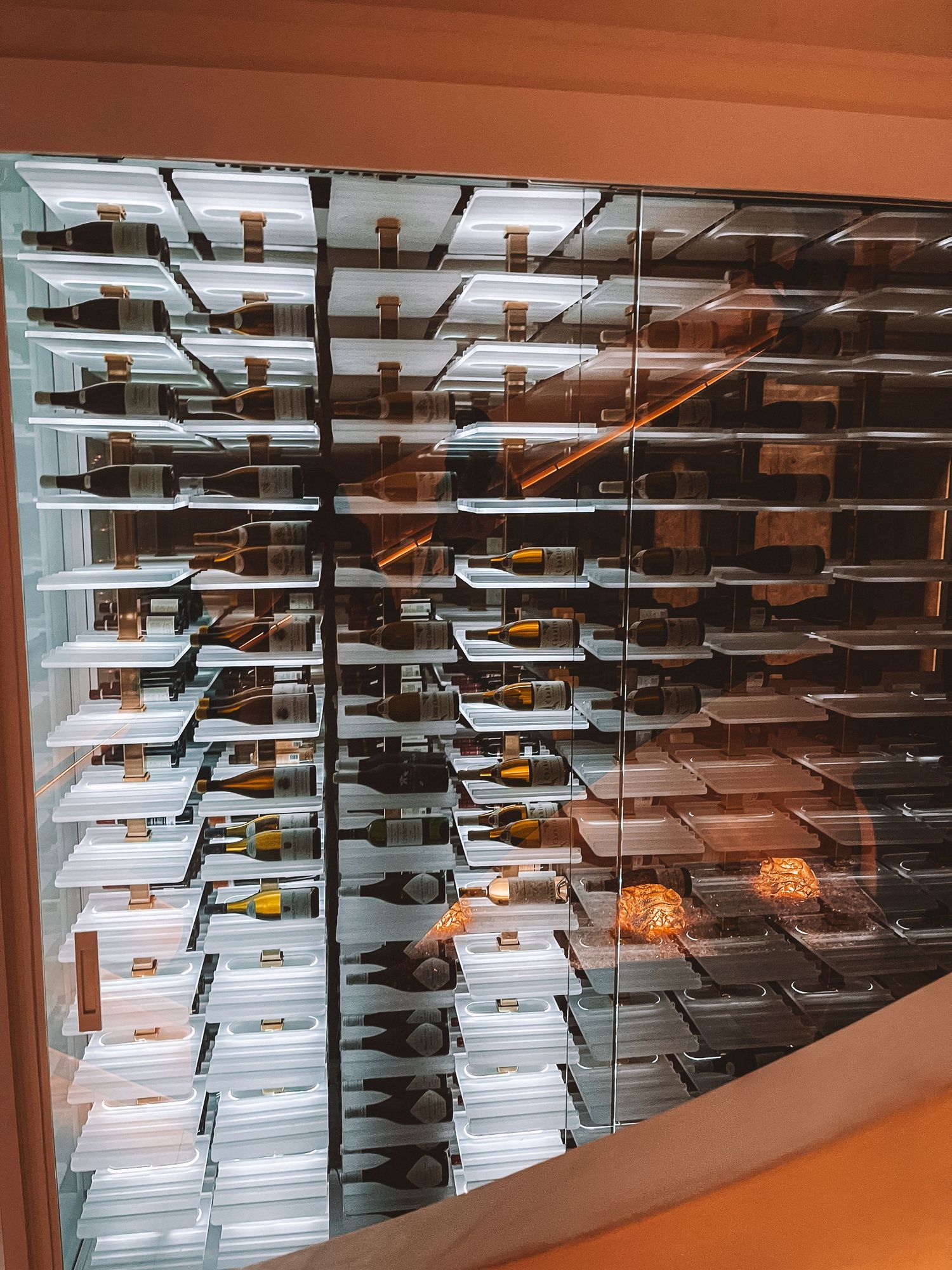 Backlit wine bottles displayed in a modern glass wine cellar at a restaurant