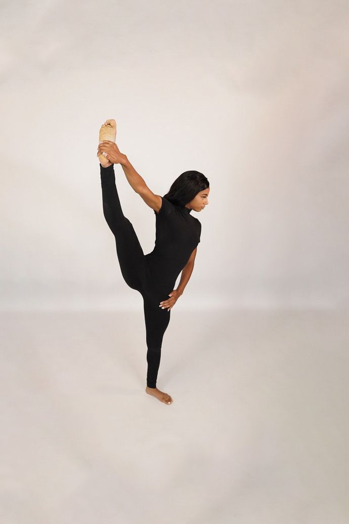 Dancer in black striking a high kick pose against a neutral studio backdrop