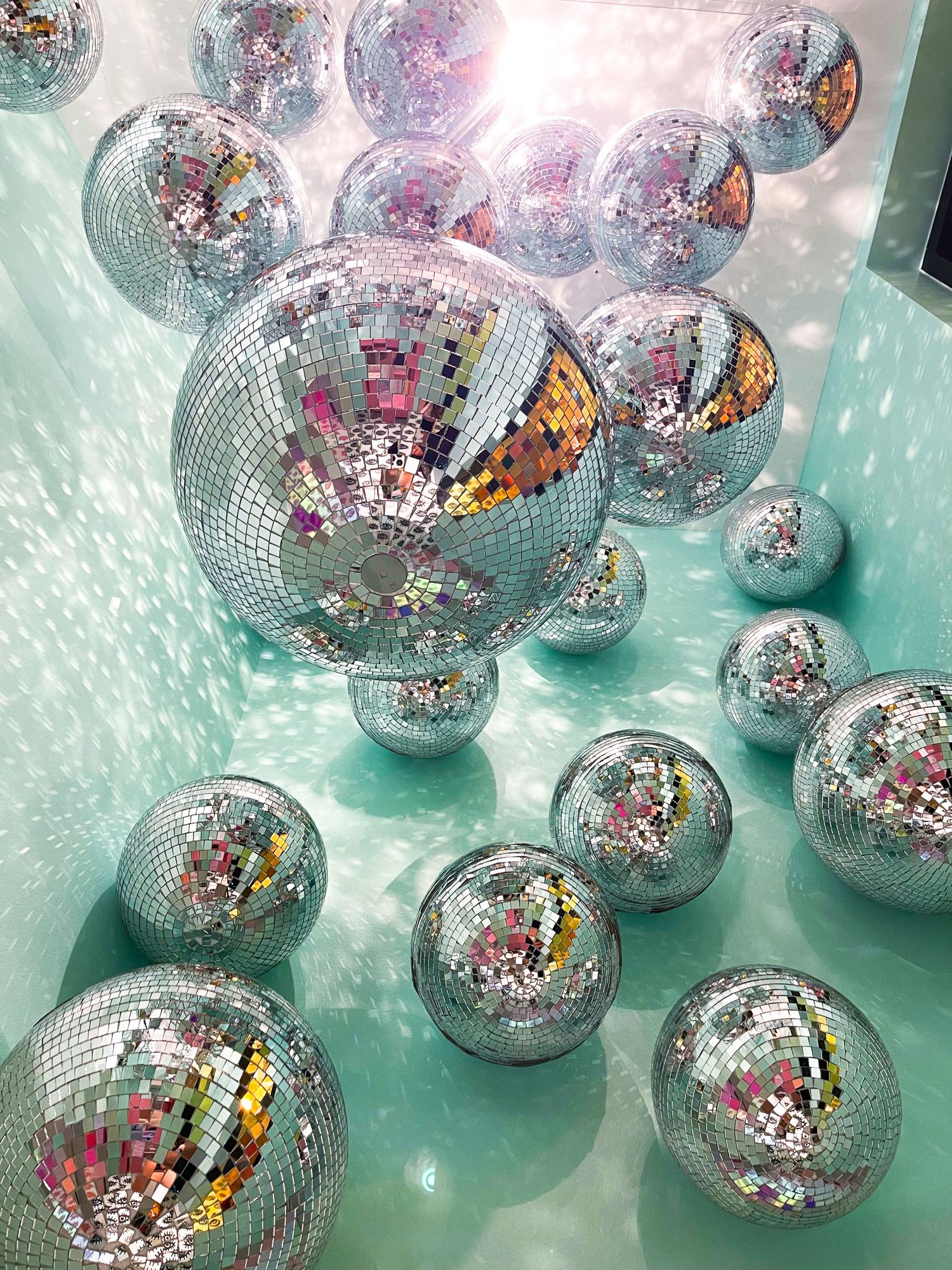 Overhead view of disco balls floating in a turquoise room with light refracting