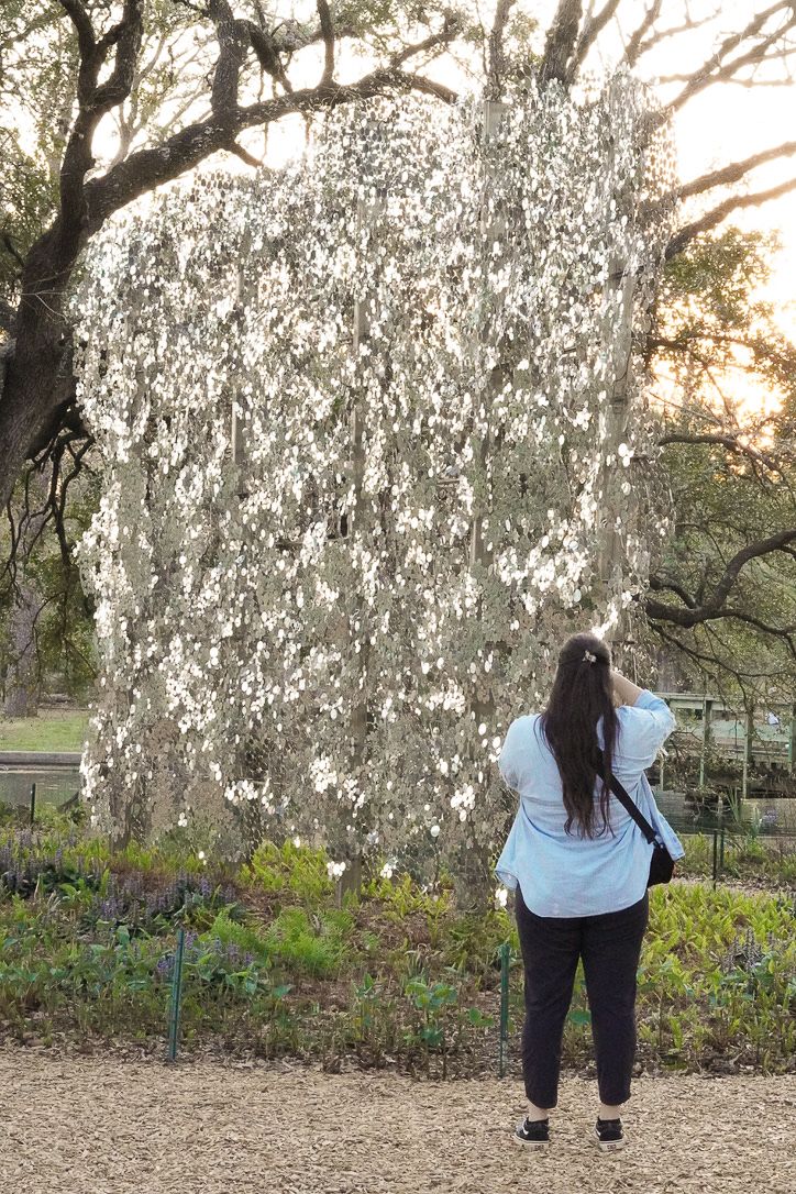 Person walking toward large metallic art installation in a park setting during golden hour