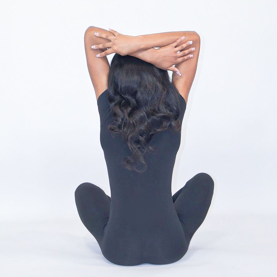 Dancer seated with arms stretched overhead, back facing the camera on a white background