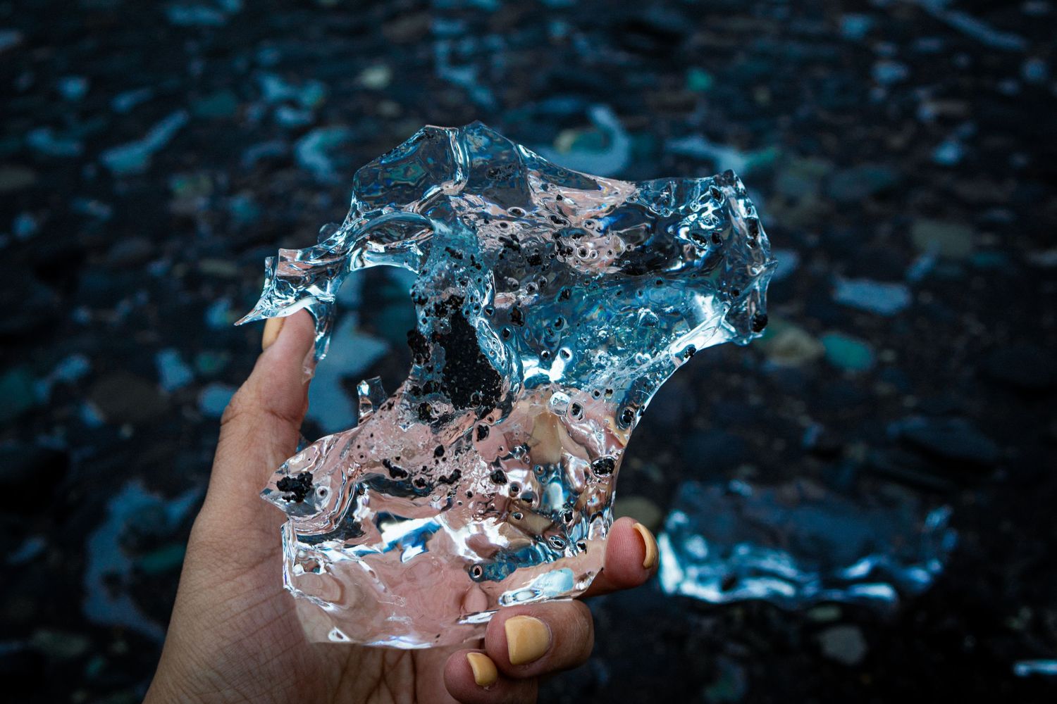 Hand holding a jagged piece of clear ice over dark, rippling water