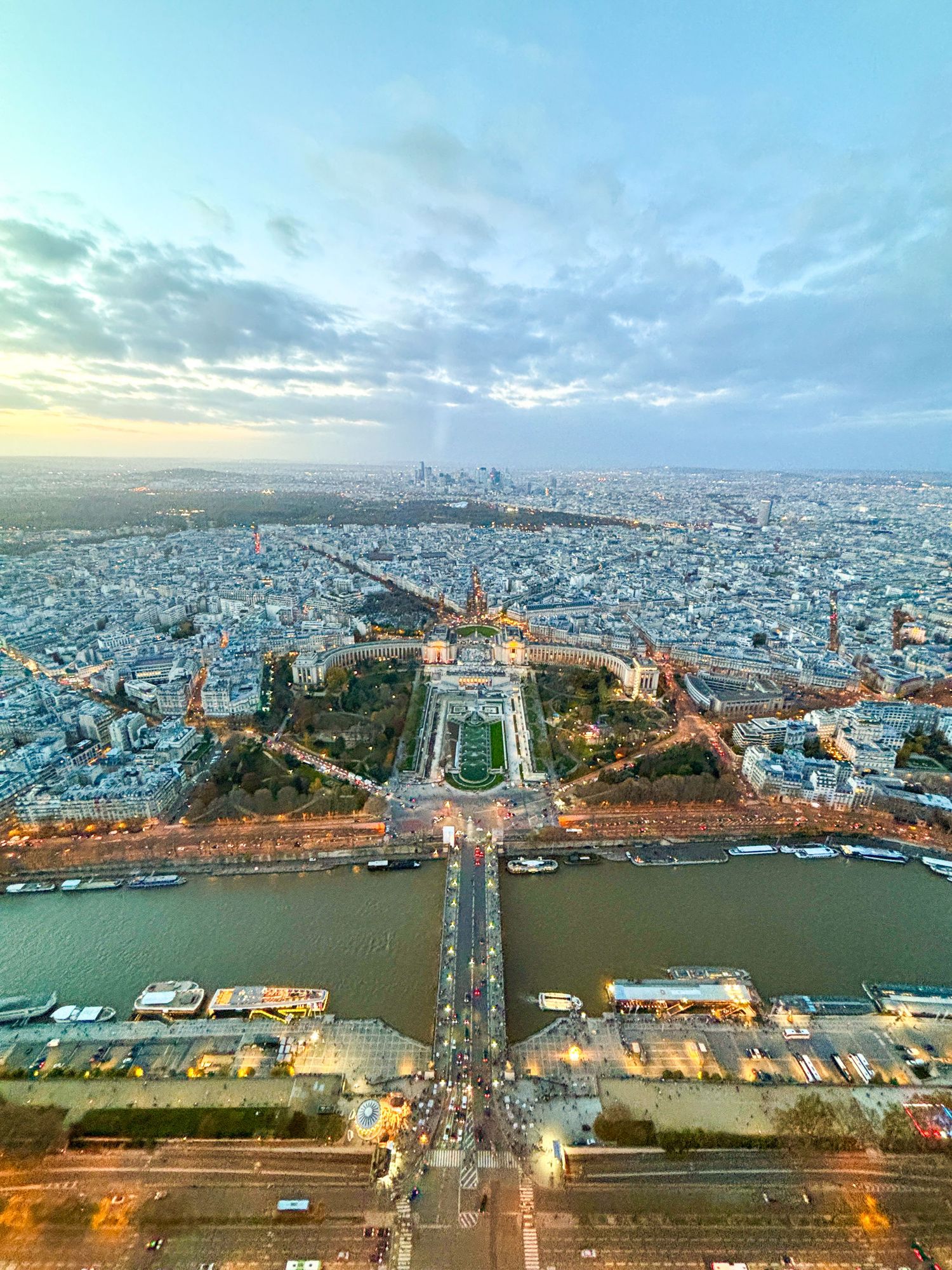 Aerial view of Paris with the Eiffel Tower centered beneath a partly cloudy sky