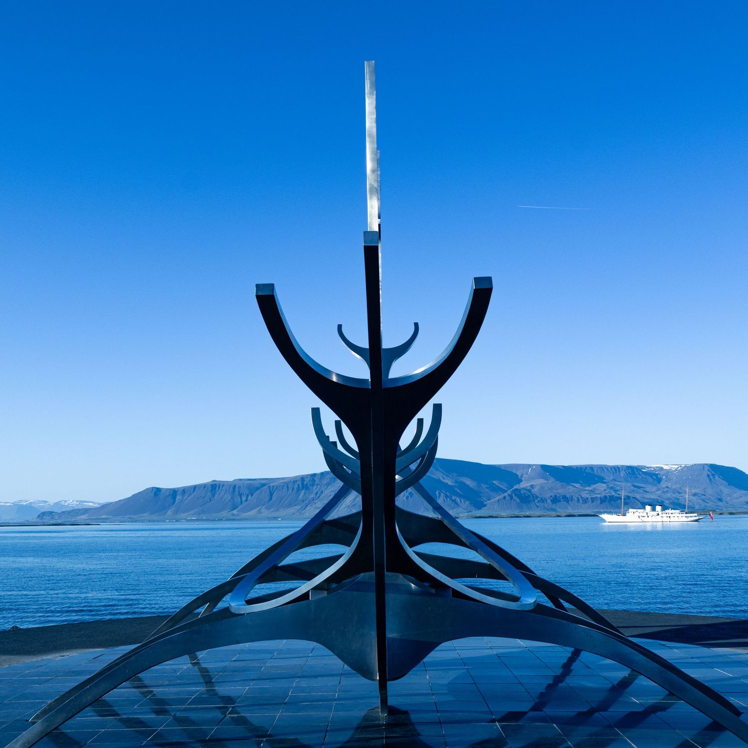 View of the Sun Voyager sculpture in Reykjavík, Iceland with clear blue skies and mountains in the distance