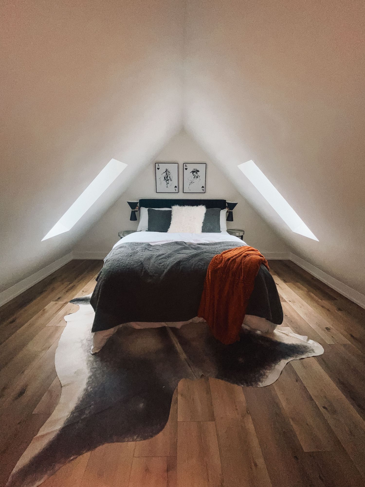 Cozy loft bed with sloped ceiling featuring hardwood floors, black bedding, orange throw blanket, and animal hide rug.