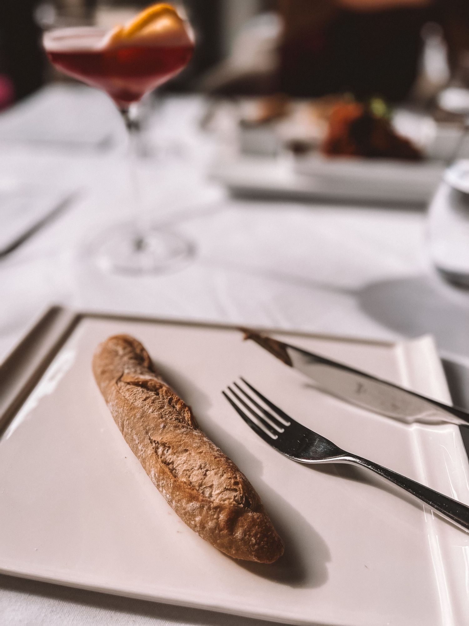 Elegant cocktail and baguette appetizer on a white tablecloth at a fine dining restaurant