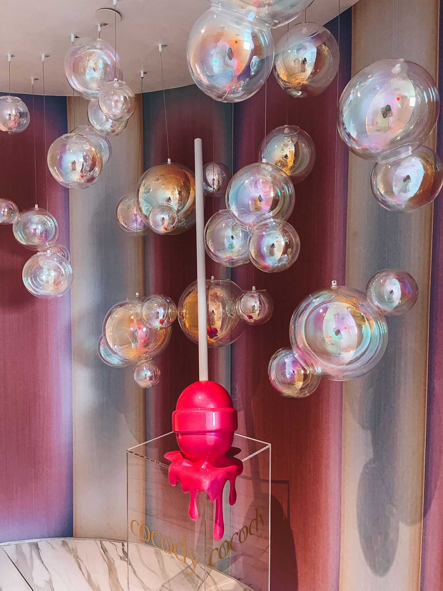 Decorative light fixture with pink bulb surrounded by floating bubbles in a whimsical hallway