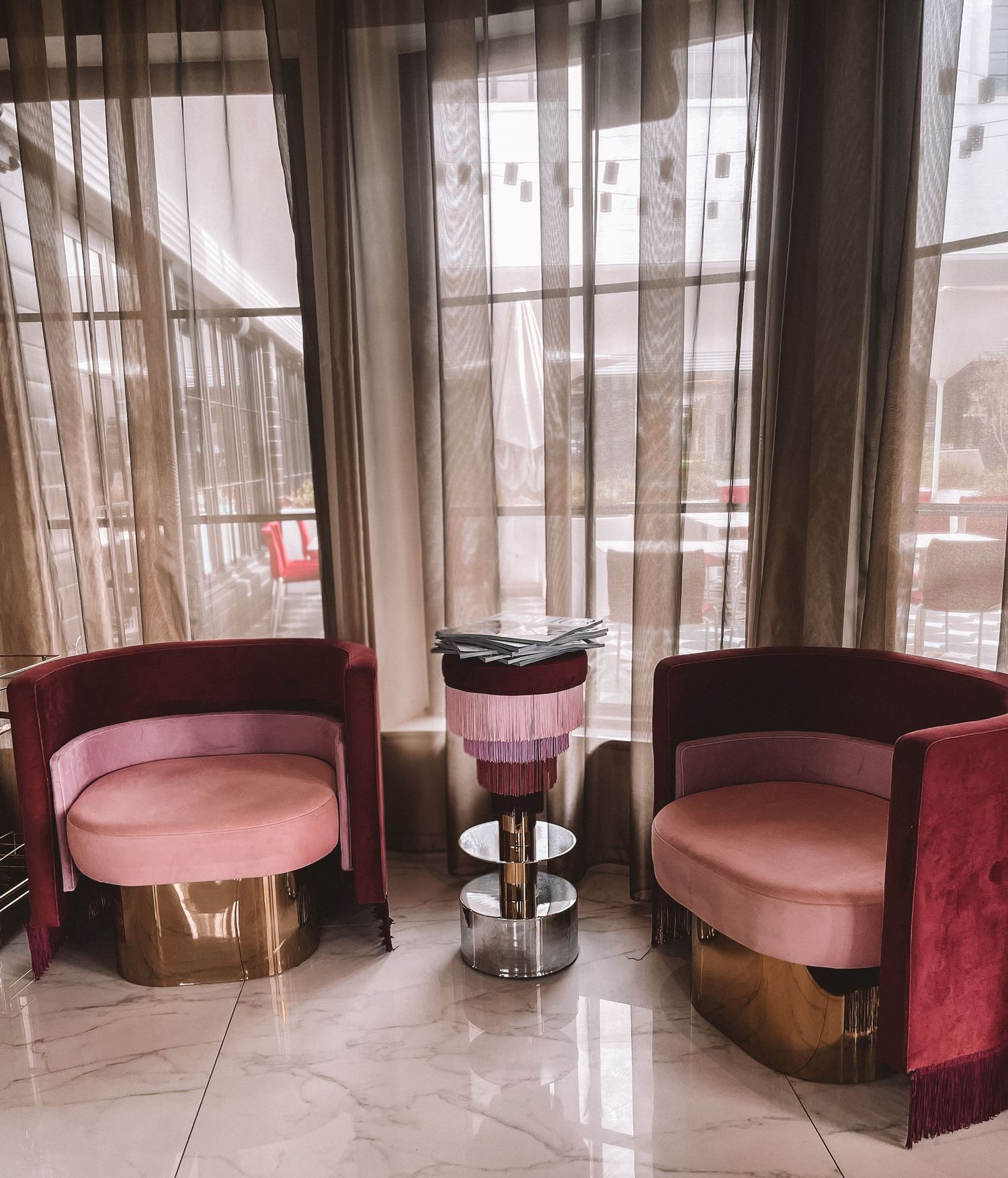 Elegant lounge area with velvet chairs and round table near large sunlit windows