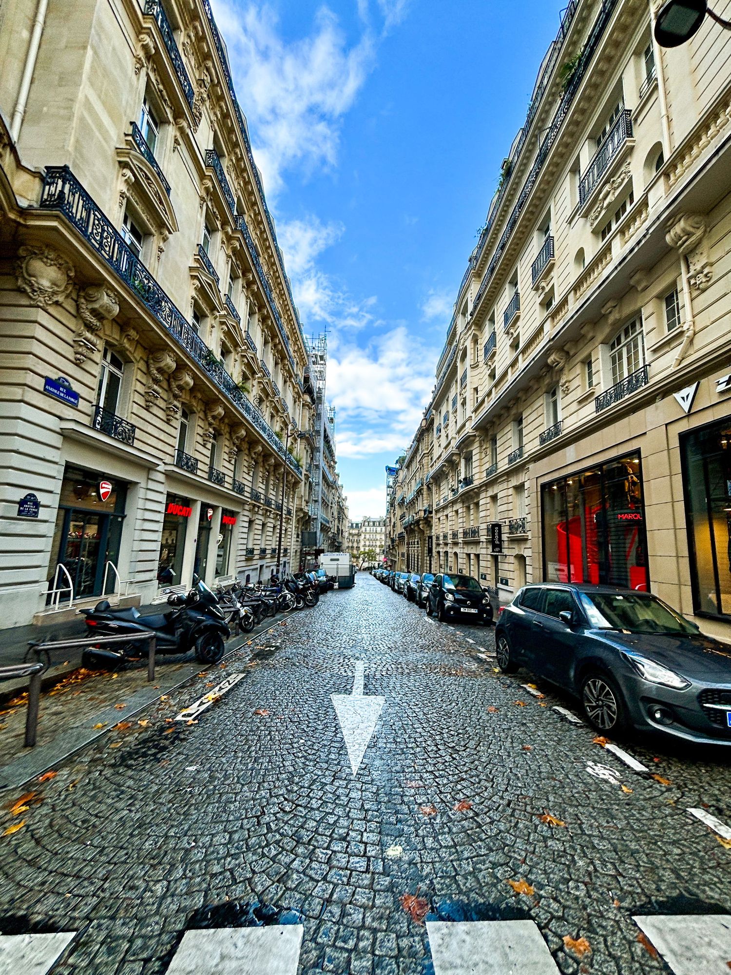 Cobbled Parisian street flanked by historic buildings and a view toward the horizon