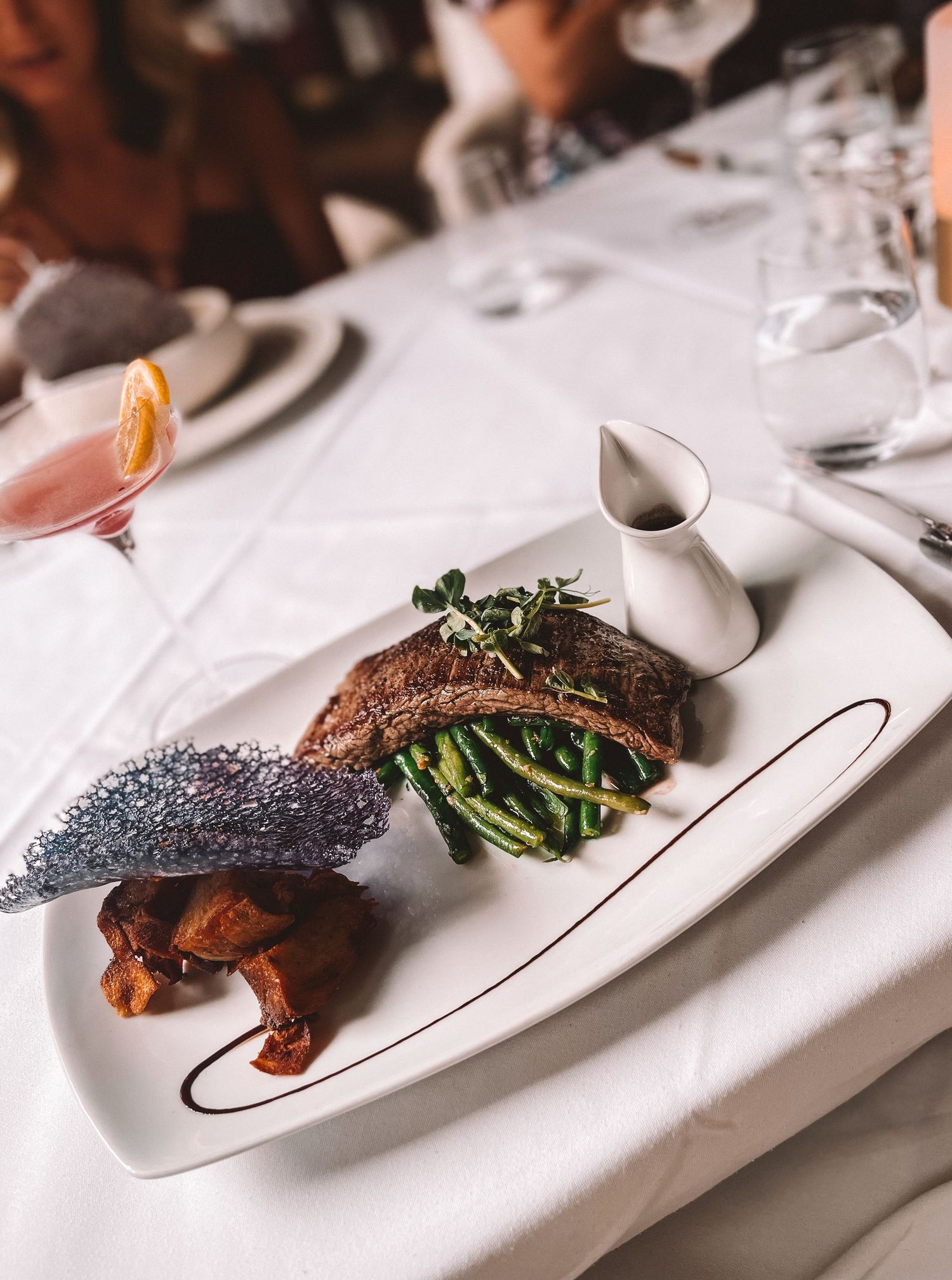 Chef plating a gourmet dish with vibrant greens and grilled protein on a white tablecloth