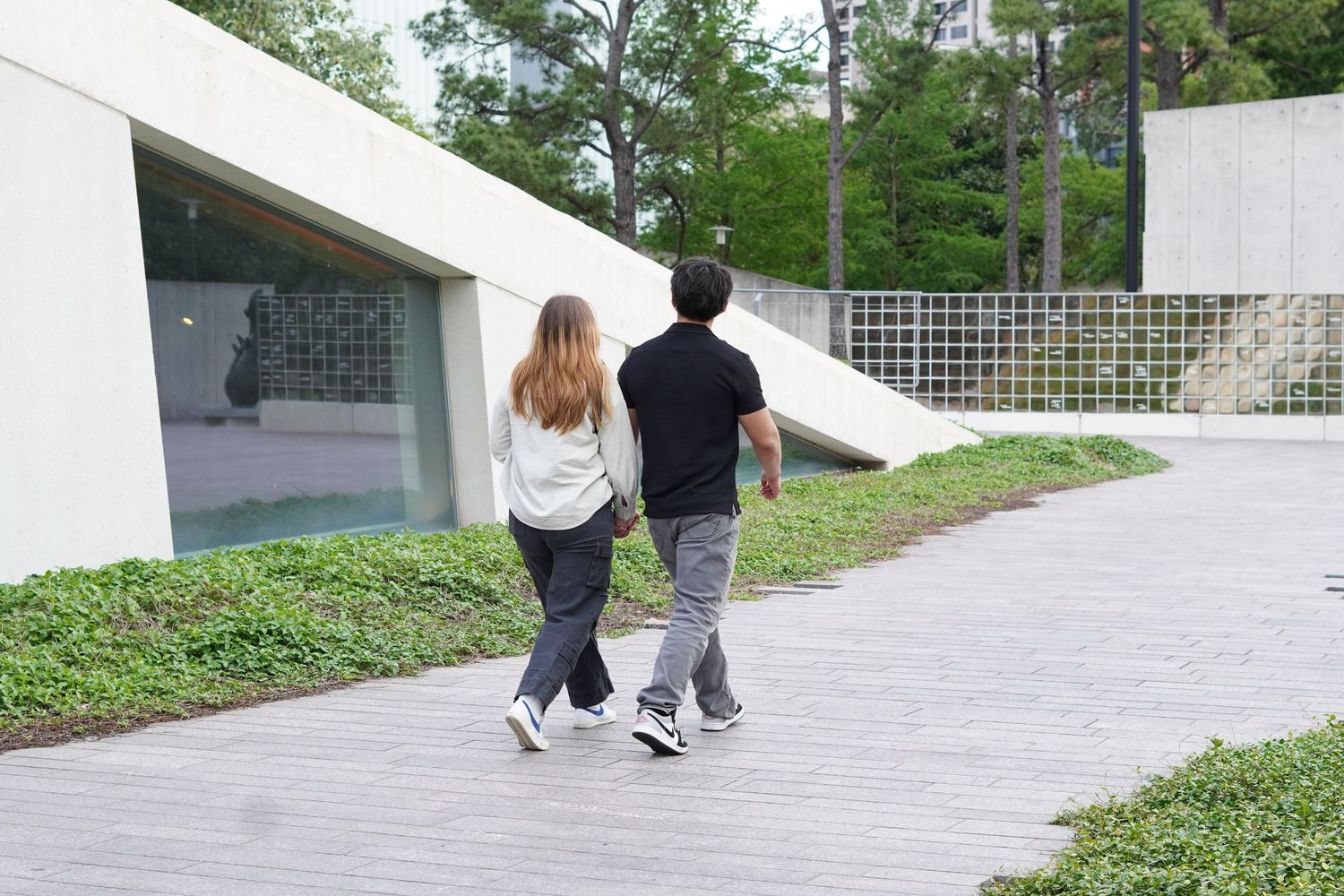 Couple walking hand in hand on a modern concrete path with greenery and architectural backdrop