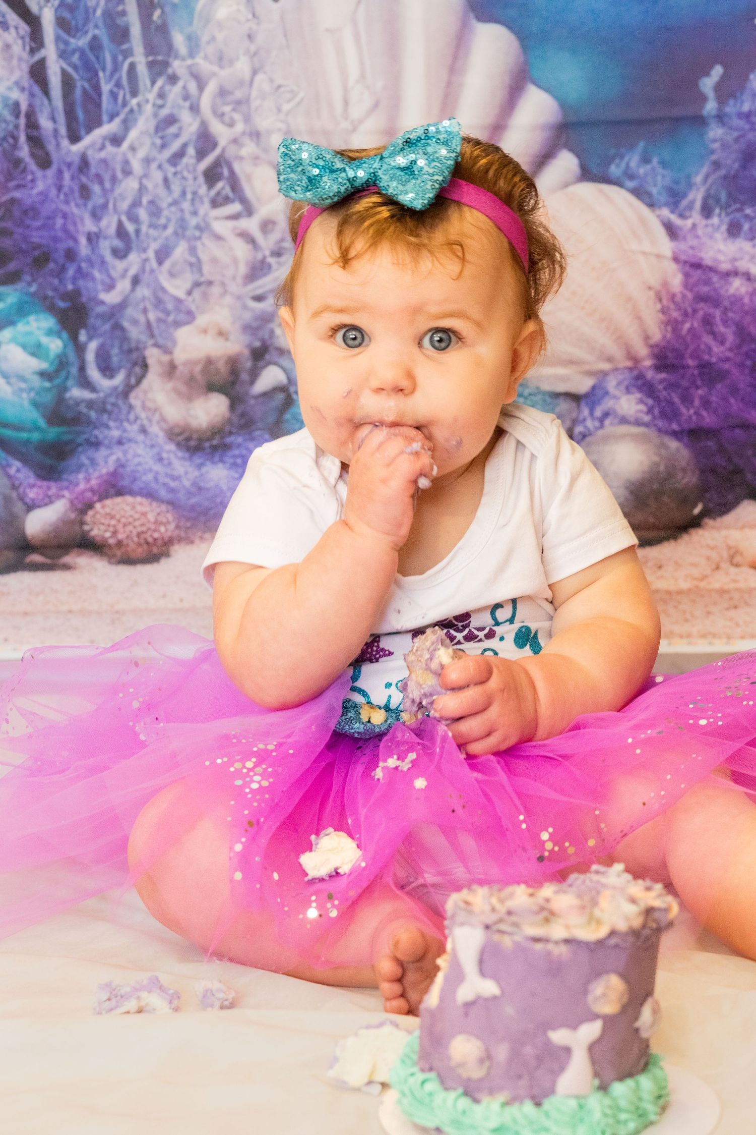Cake smash photo session setup with pink tutu and purple backdrop.