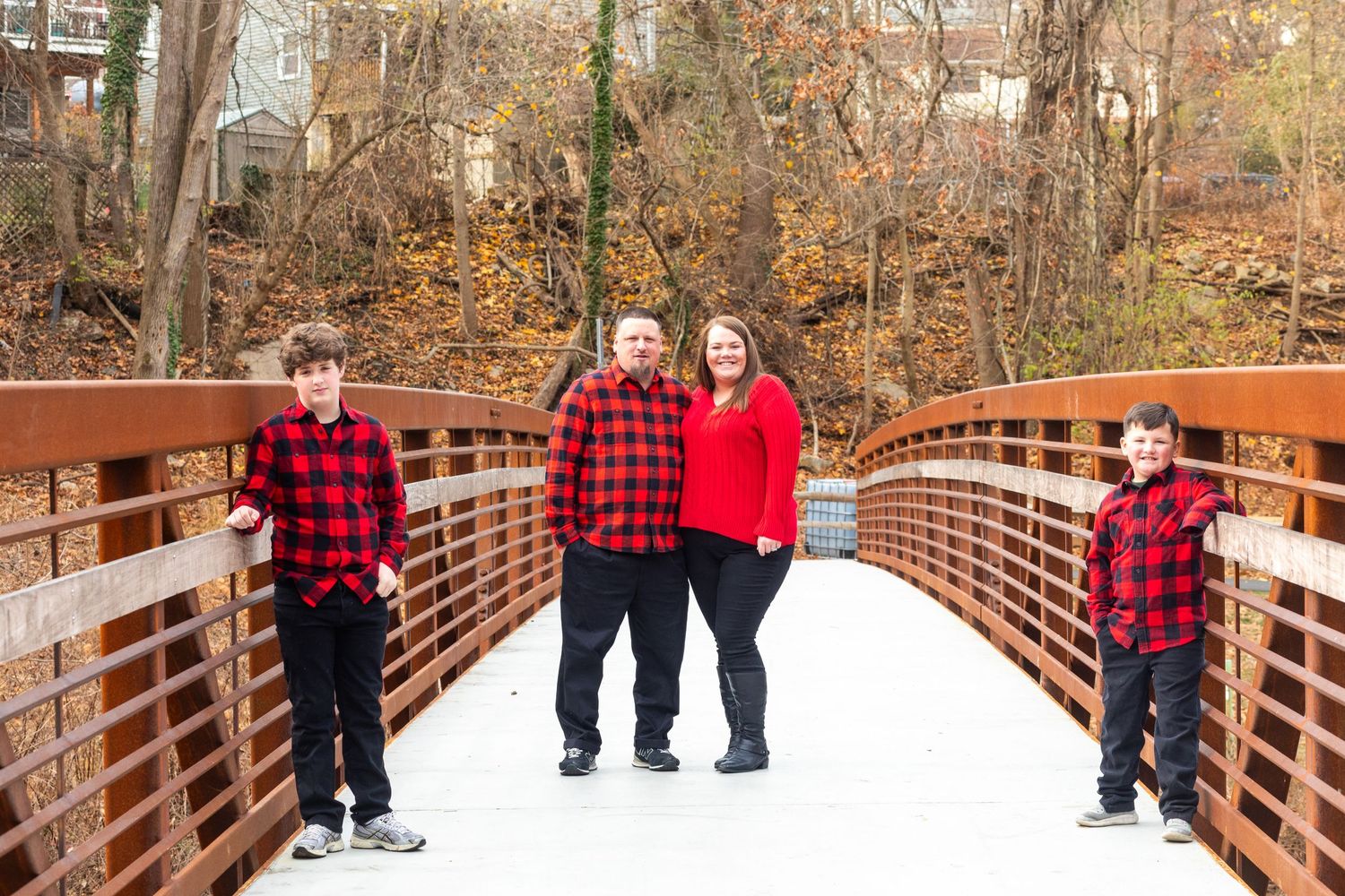 Family wearing matching buffalo plaid outfits on wooden bridge in winter.