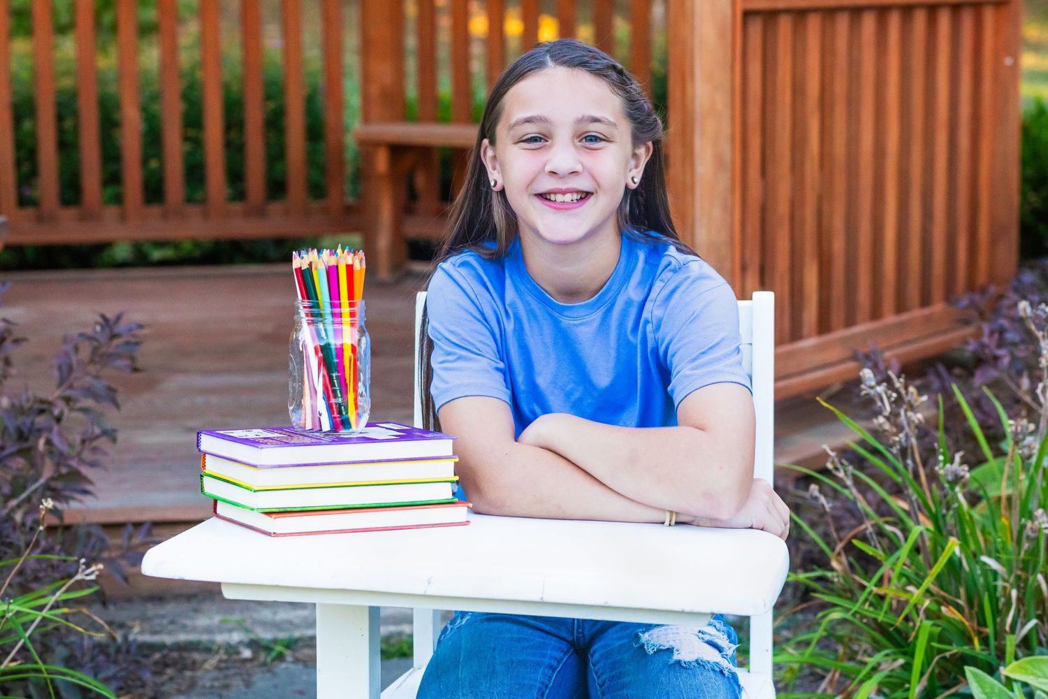 Student sitting at desk with books and pencils on outdoor wooden deck.