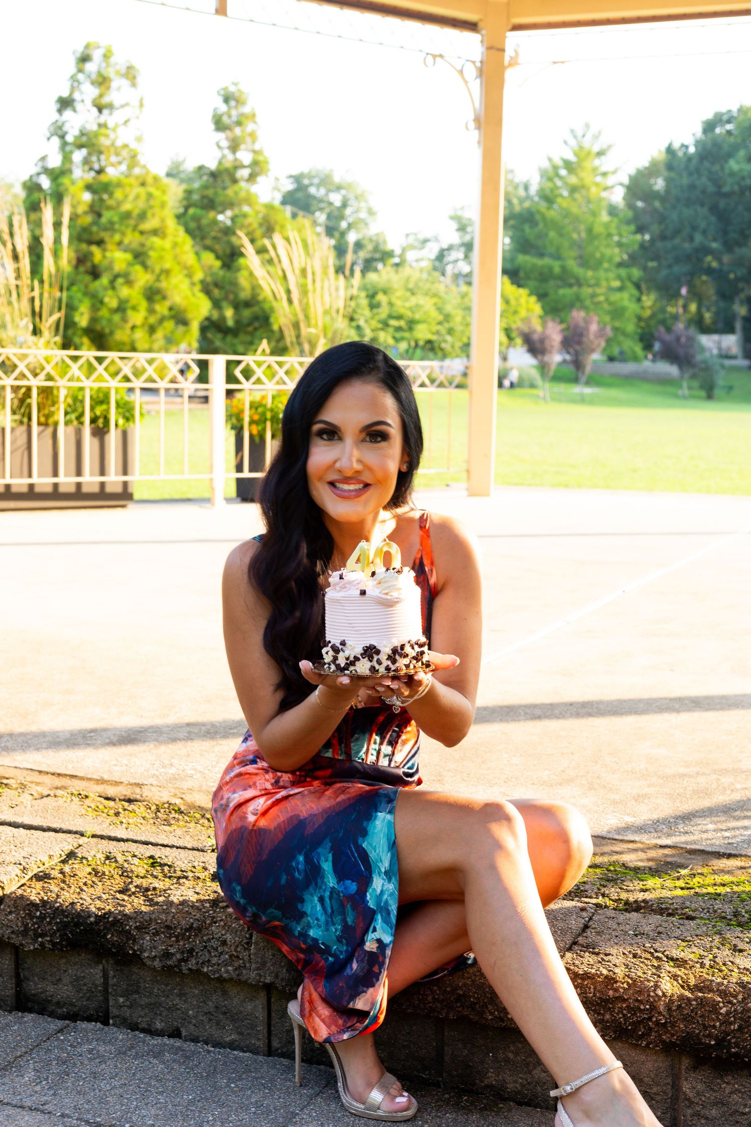 Woman in colorful dress holding dessert while sitting outdoors under pavilion.