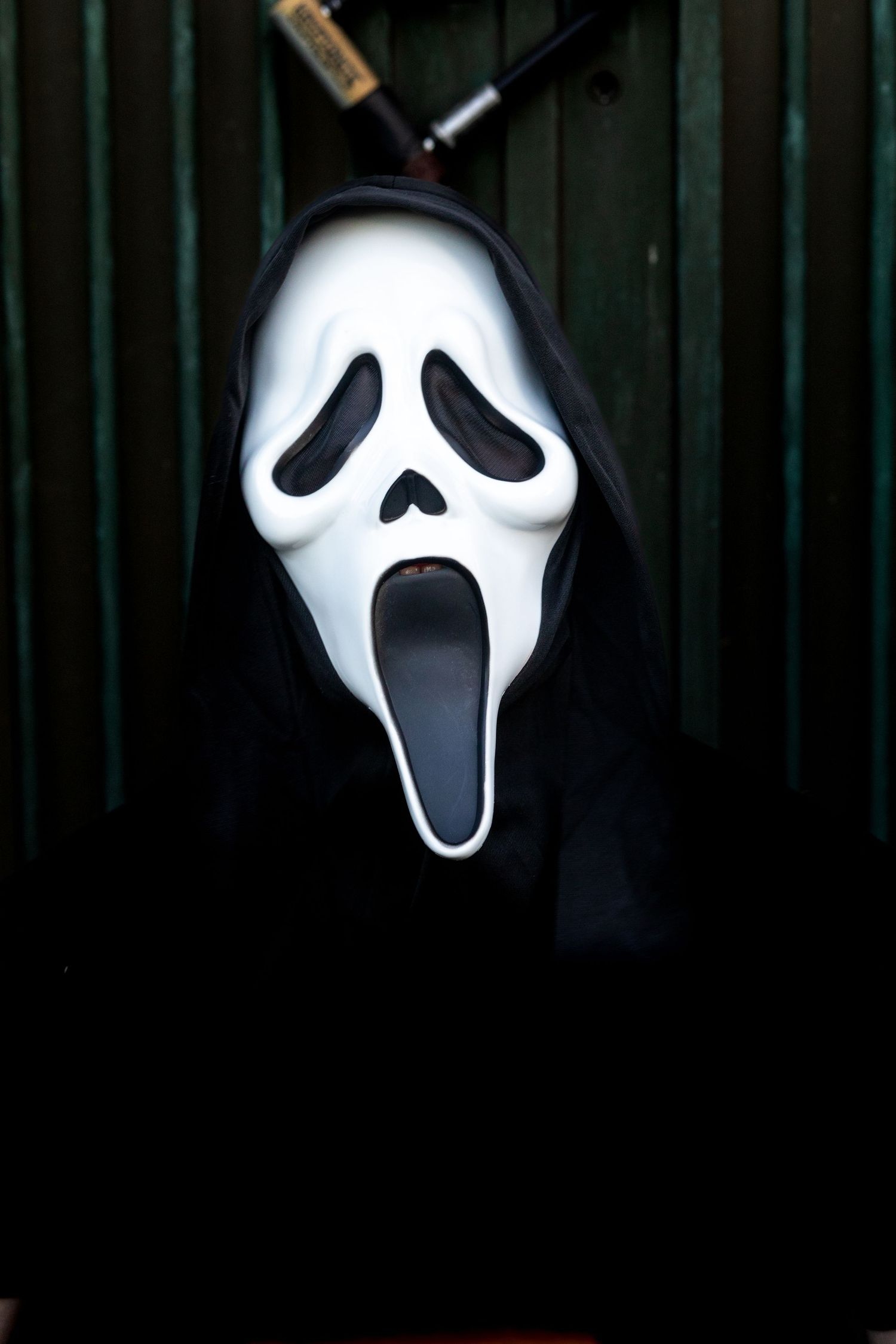 A classic Ghostface mask from the Scream movie franchise shown against a dark background.
