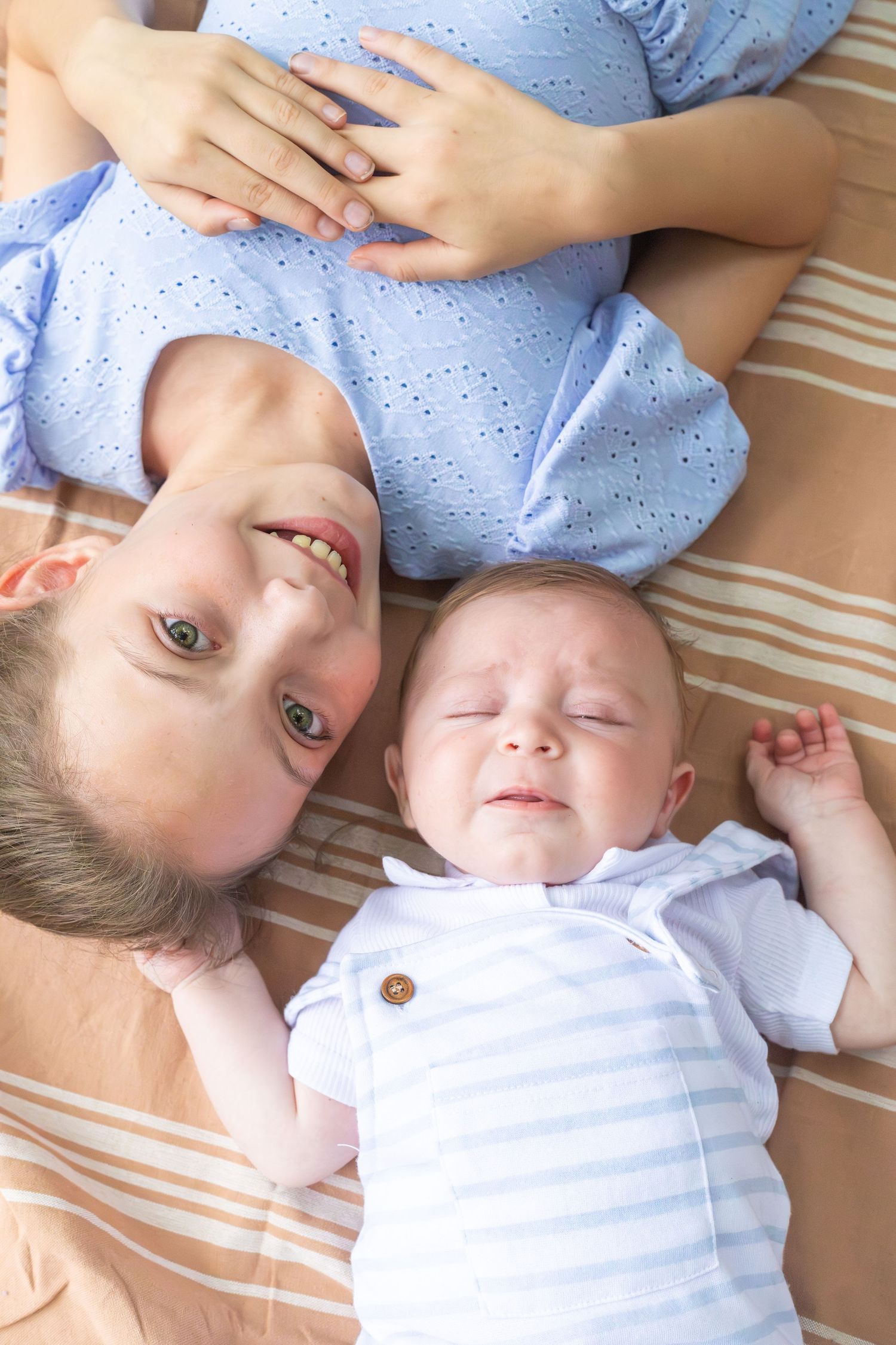 A parent and baby lie together on striped bedding while resting and making eye contact.
