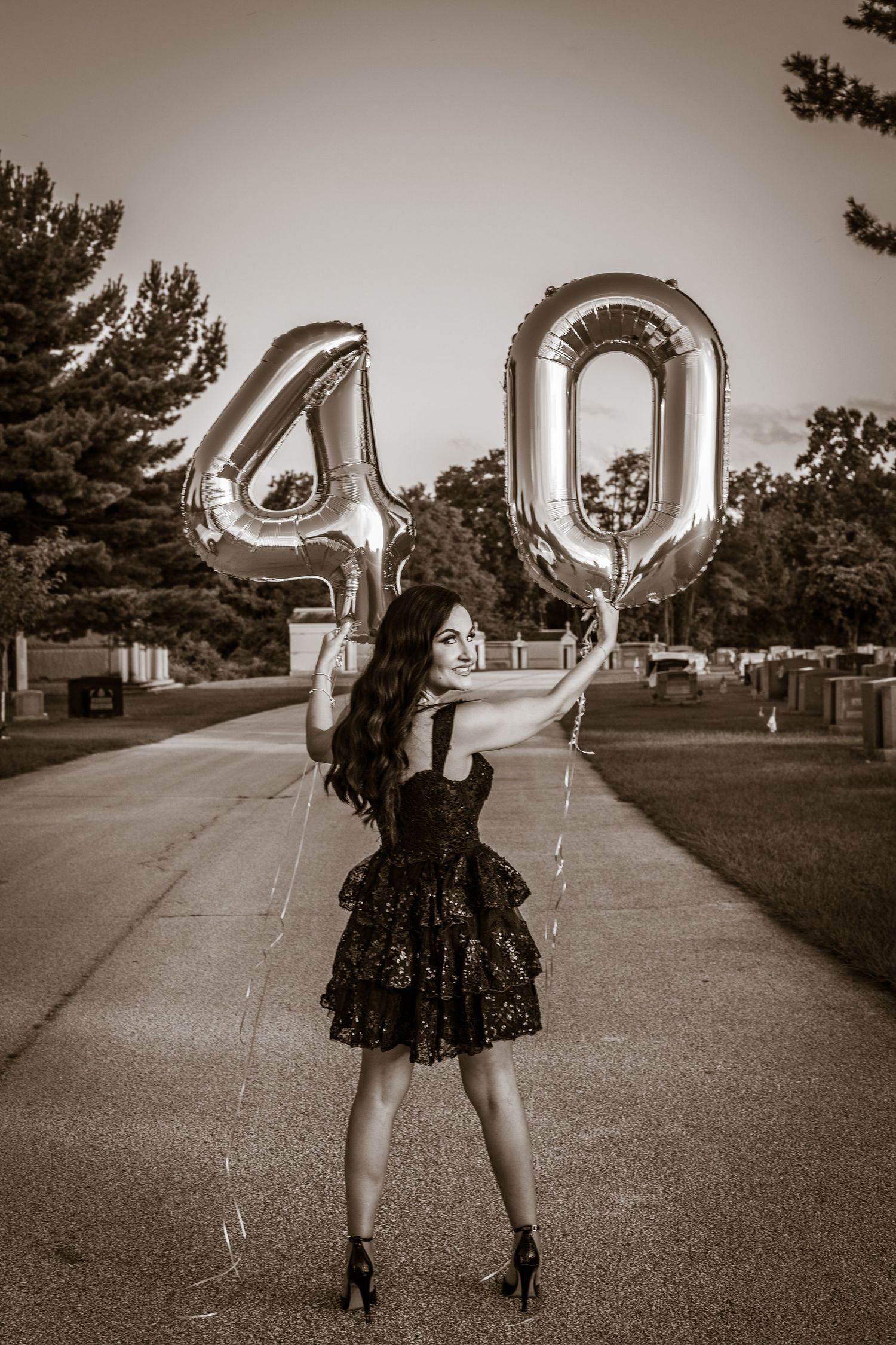 Person in black dress holds silver number 40 balloons outdoors for milestone celebration photo.