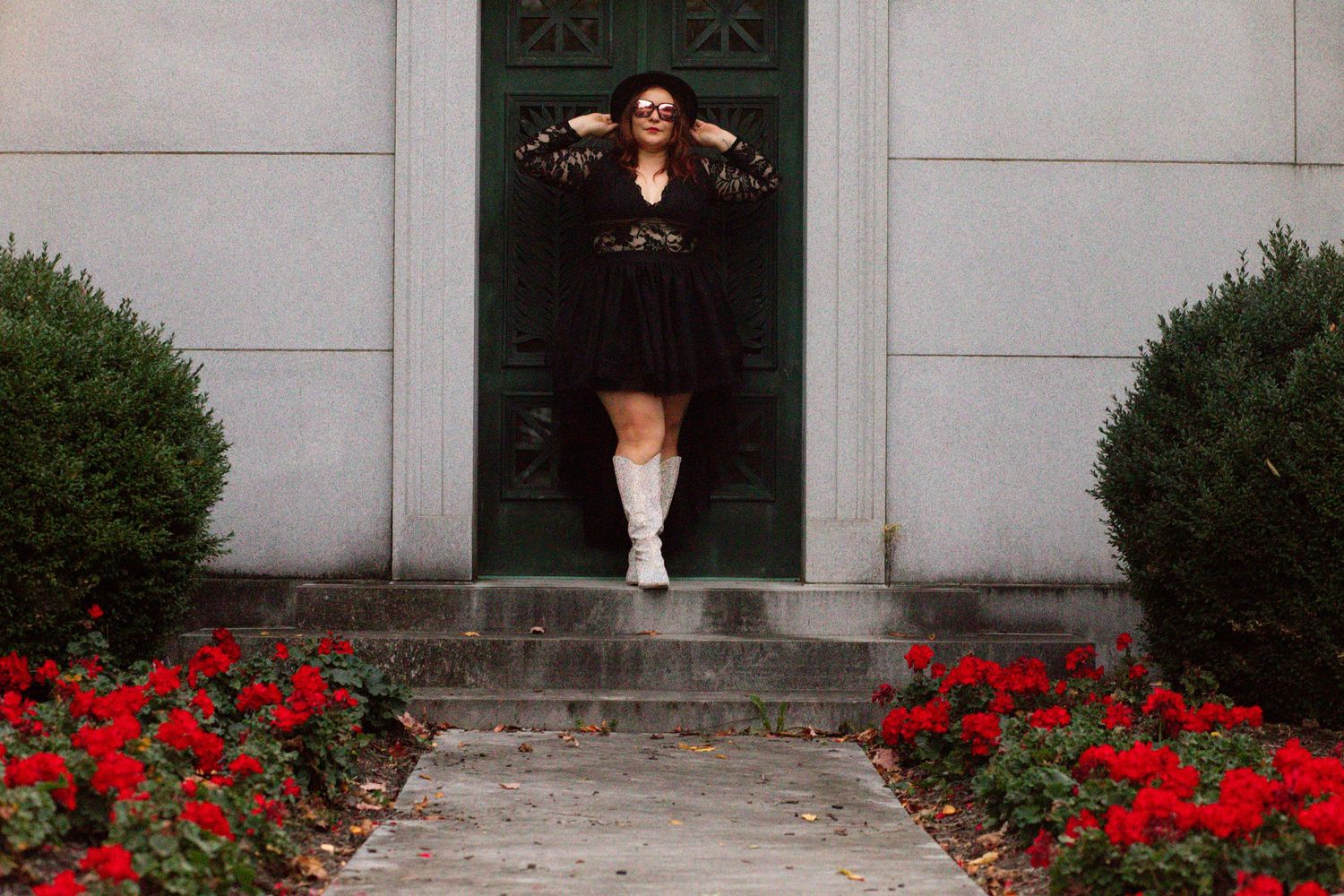 A figure in a black outfit jumps in a doorway framed by stone steps and red flowers along the path.