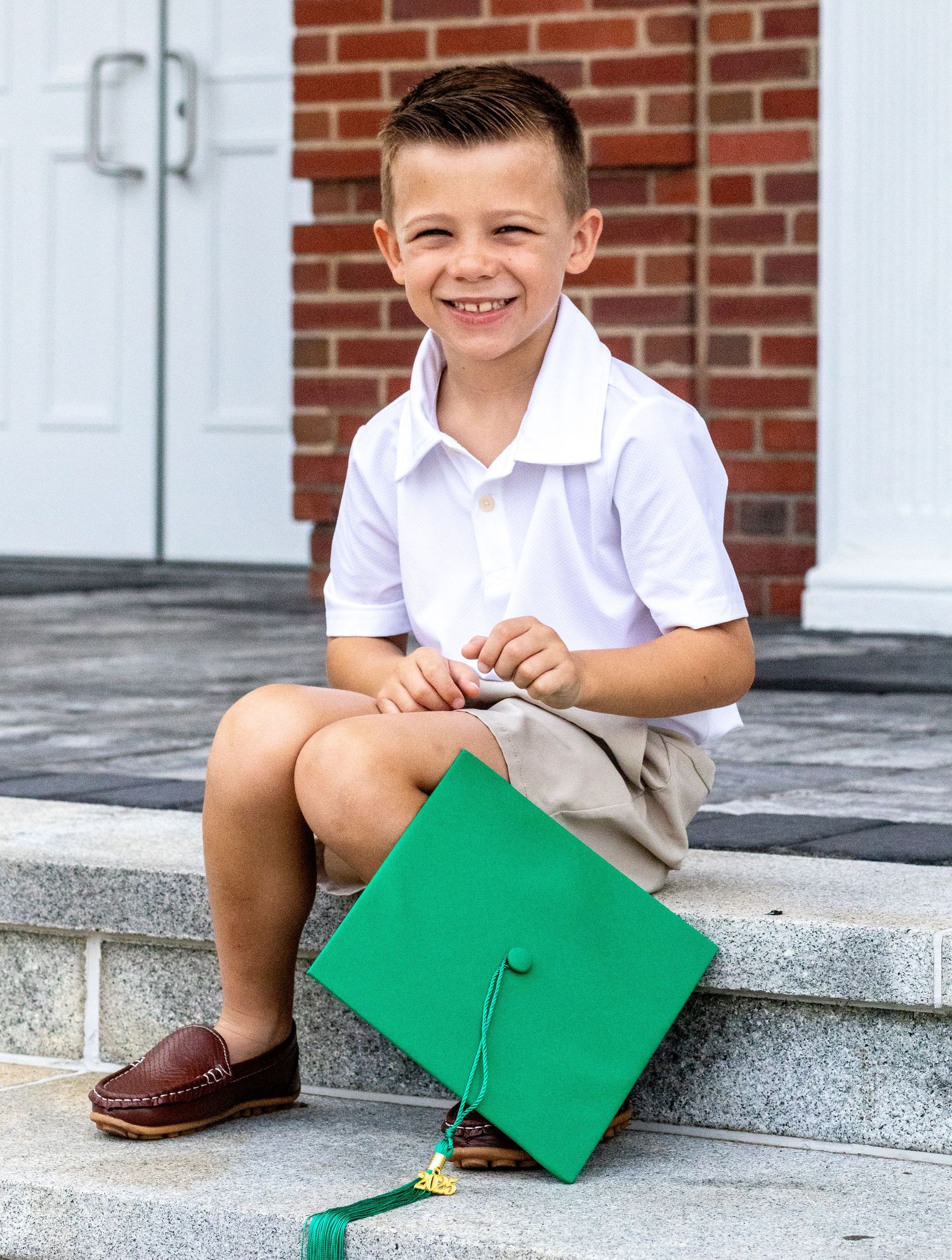 Green graduation cap on stone steps with brick building background.