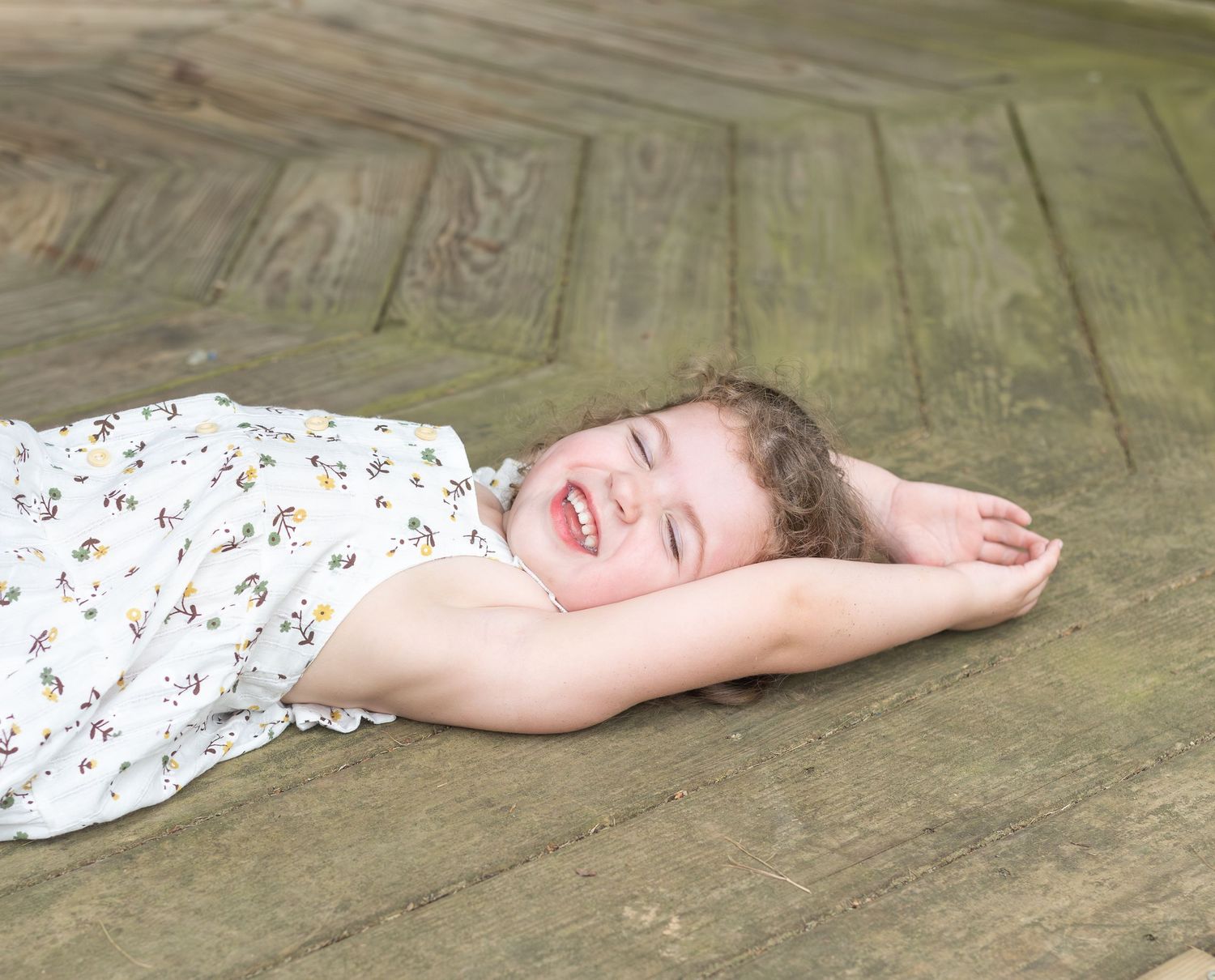 A small child lies sleeping peacefully on a weathered wooden floor while wearing a floral print dress.