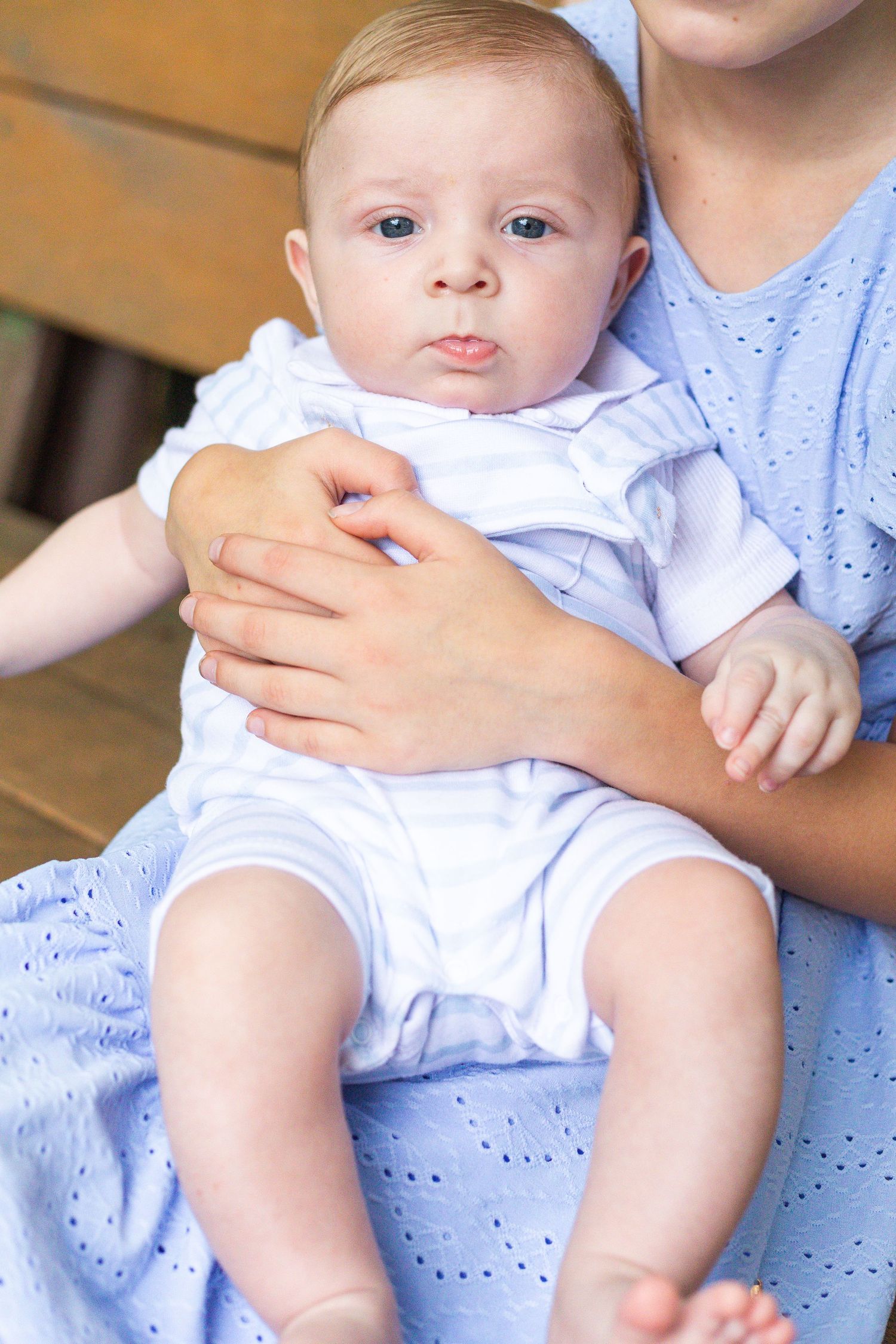 A baby in a white outfit sits on someone's lap wearing a soft blue dress or garment in a sequential photo series.