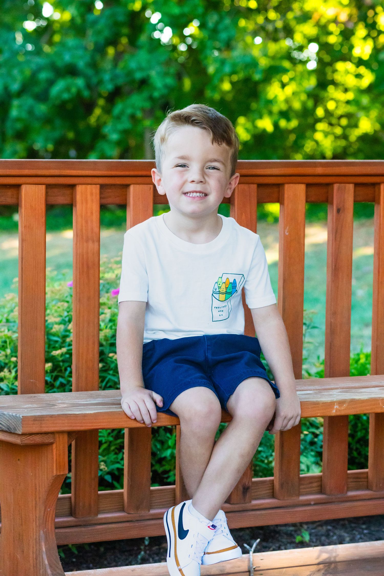 Young child sitting on wooden deck railing wearing white t-shirt and blue shorts.