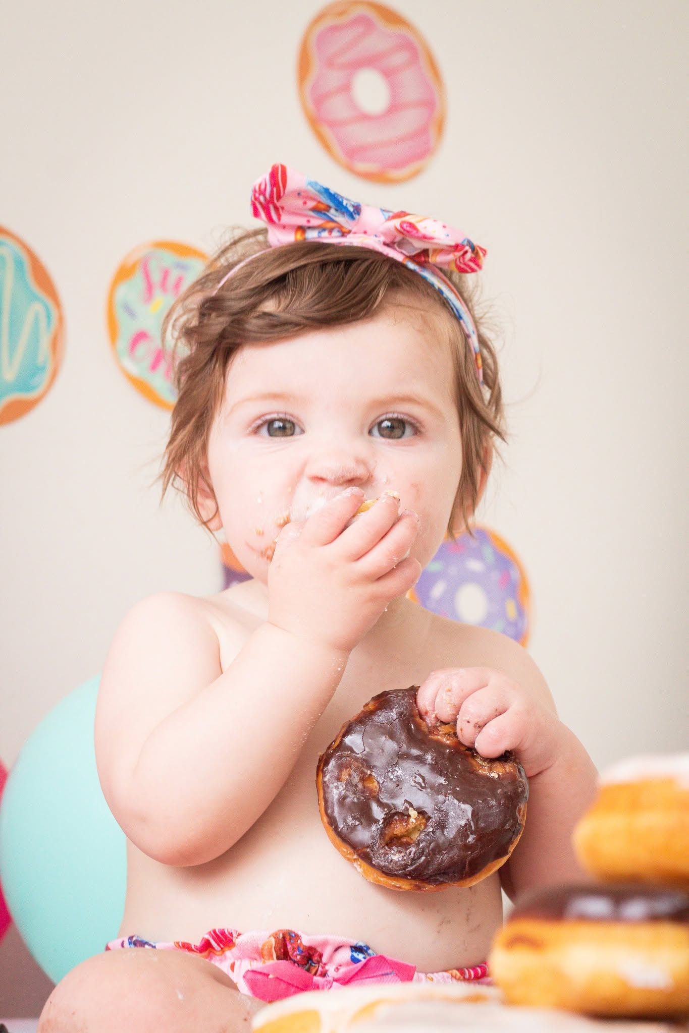 Baby with chocolate-covered face enjoying a donut against white background.