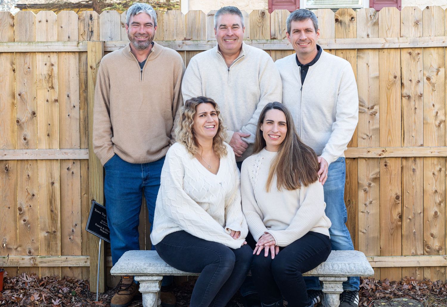 Family group poses together on wooden bench in front of privacy fence.