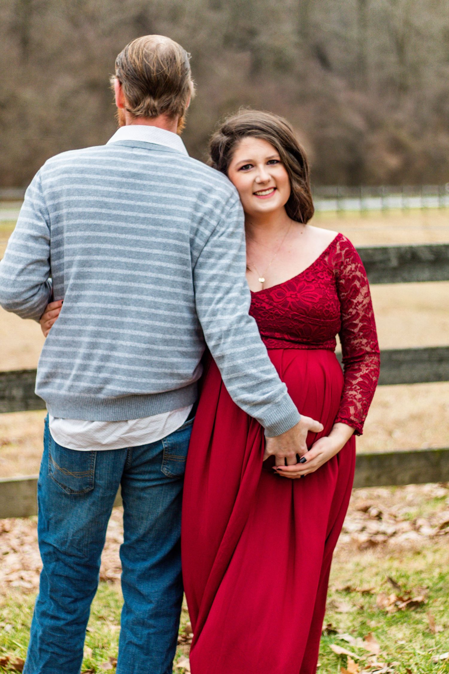 Couple in casual attire standing by wooden fence during countryside photoshoot.