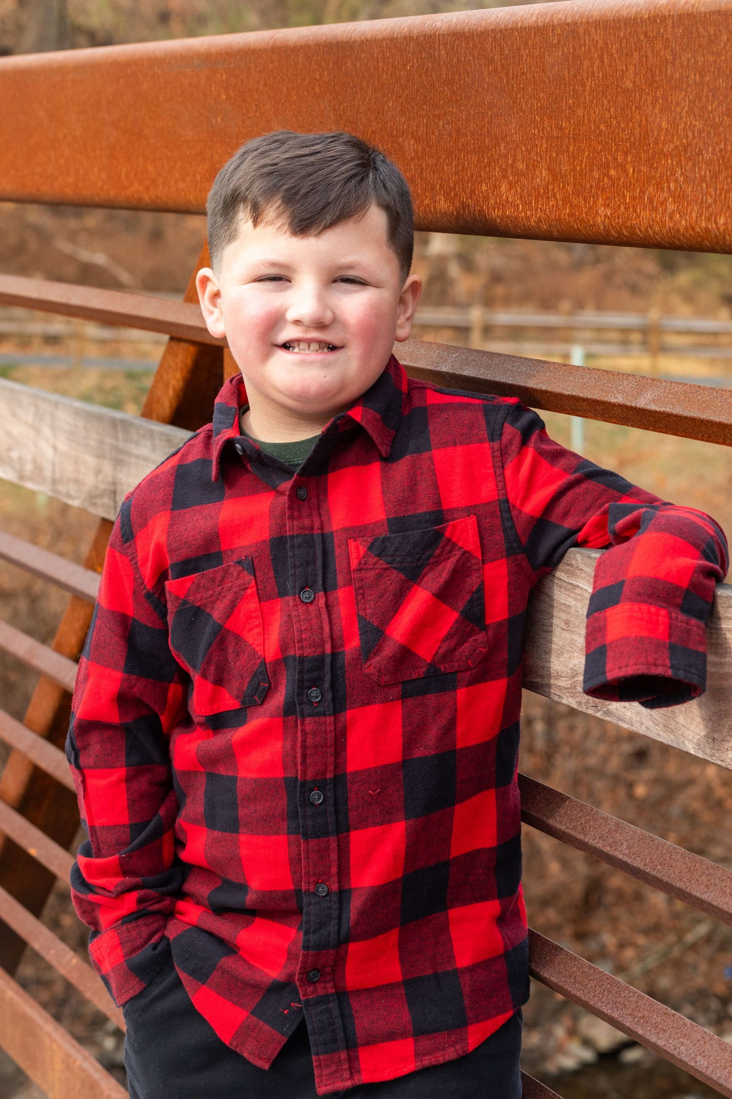 Child in red and black plaid flannel shirt leaning against wooden bench outdoors.