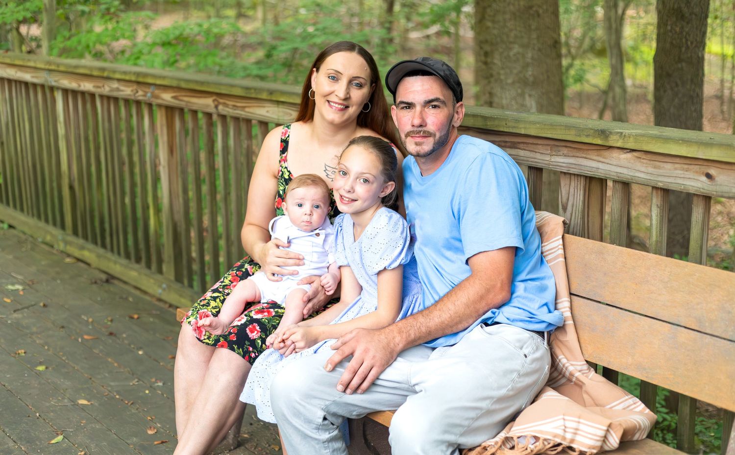 A family sitting together on a wooden boardwalk path through a lush wooded area.