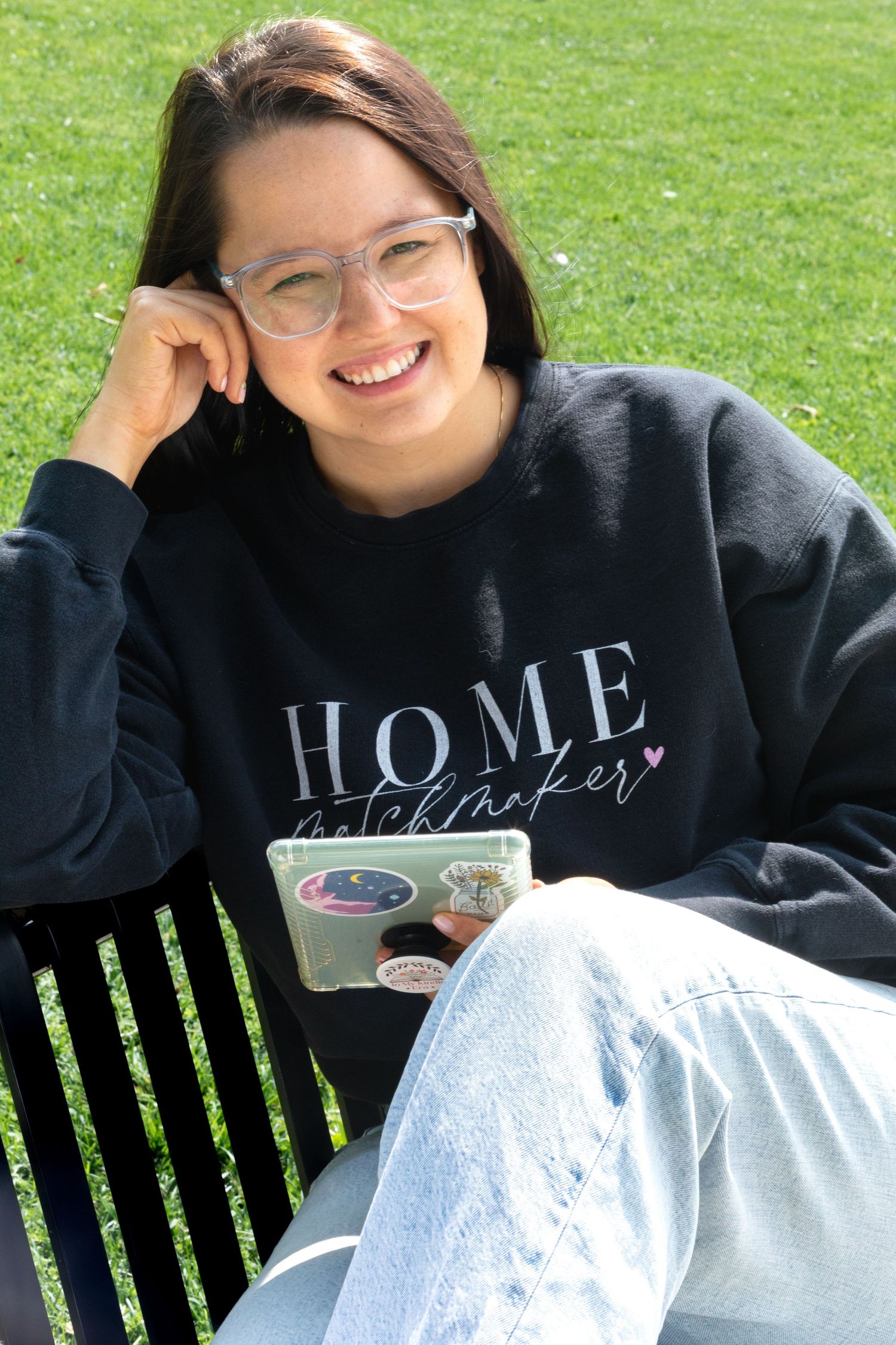 Person wearing black HOME sweatshirt relaxes on park bench with coffee.