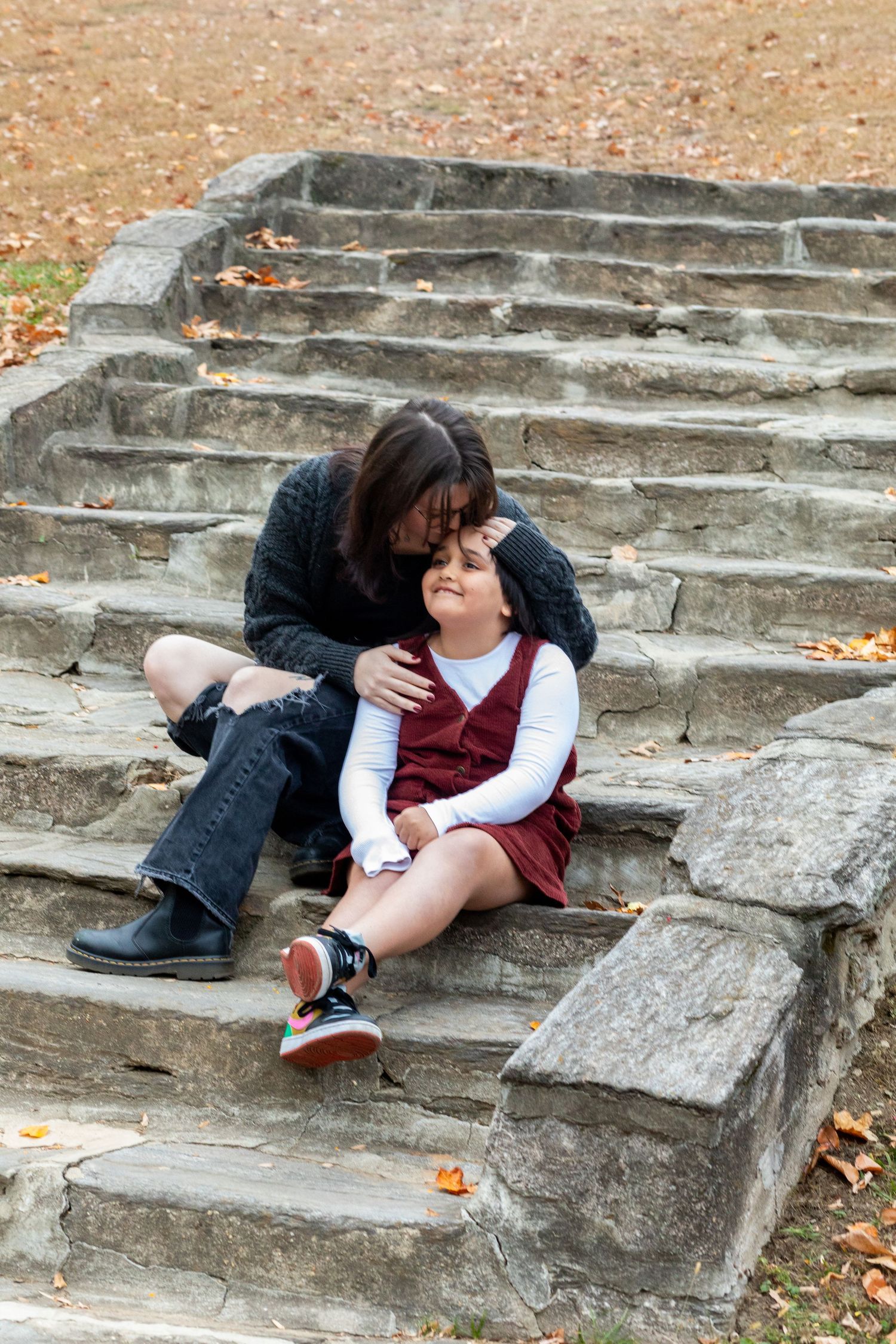 Child sitting on rustic stone steps during autumn photoshoot.