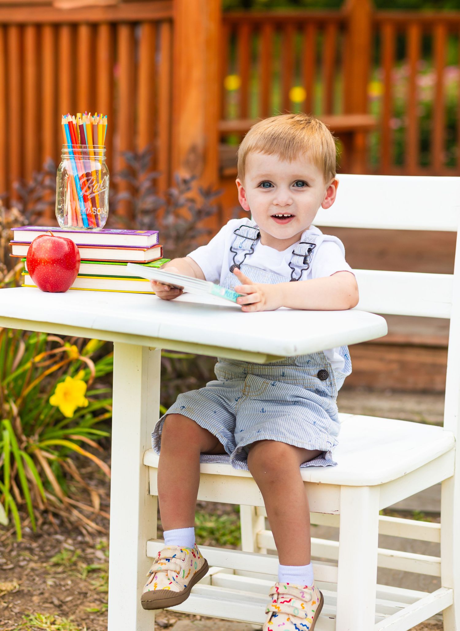Child sitting at white outdoor furniture with books and art supplies.