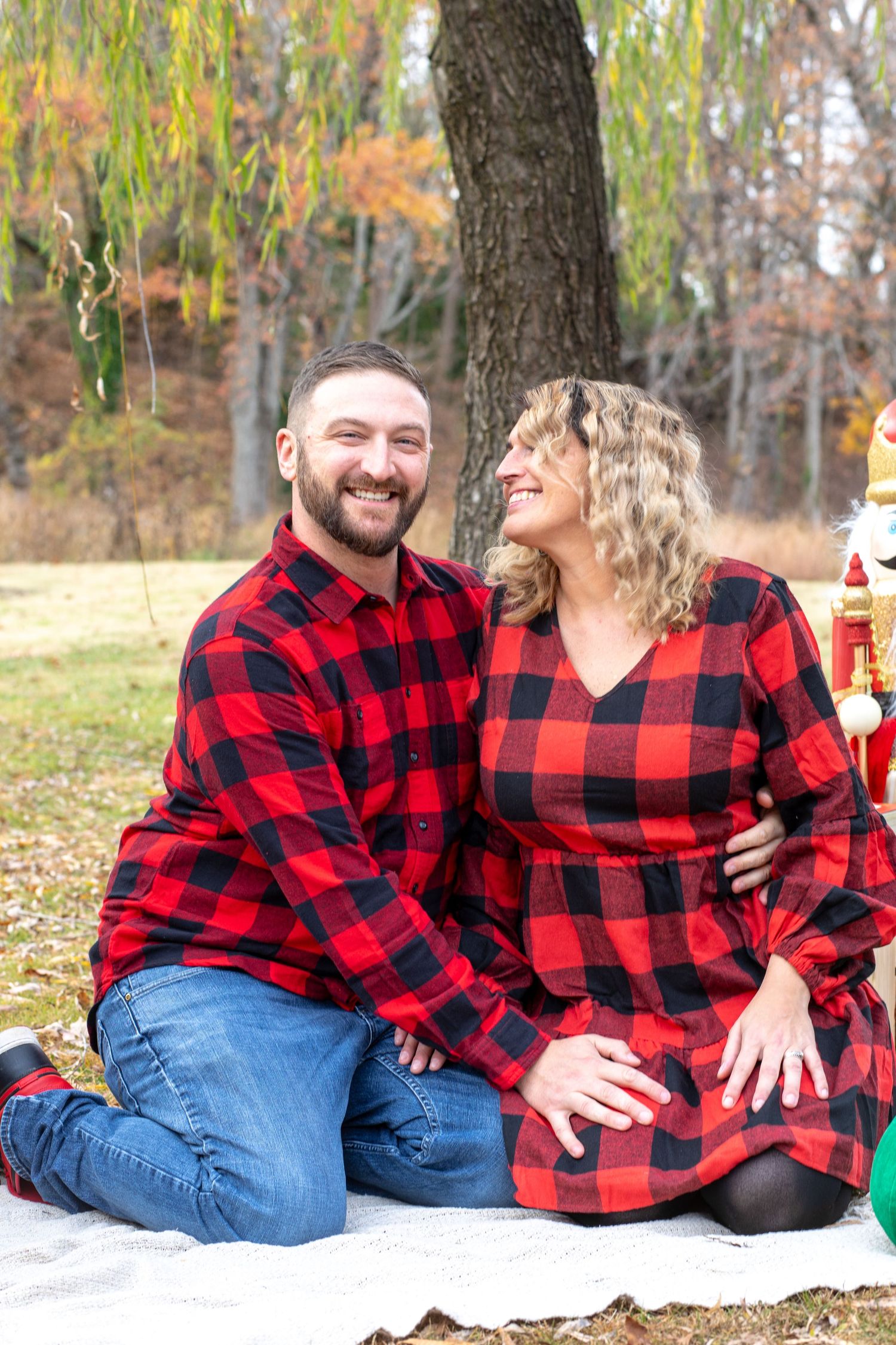 Couple in matching buffalo plaid shirts sits together on blanket during autumn photoshoot.