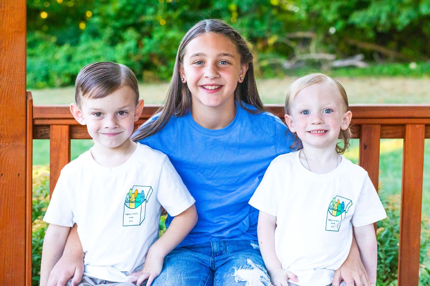 Family members in white and blue shirts sit together on a wooden deck surrounded by greenery.